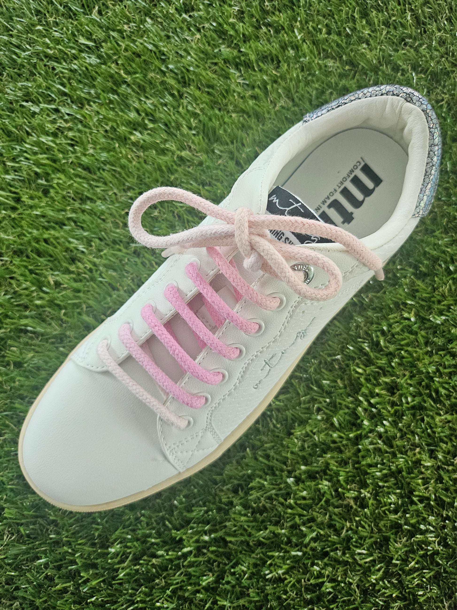 White sneaker with pink laces on grass