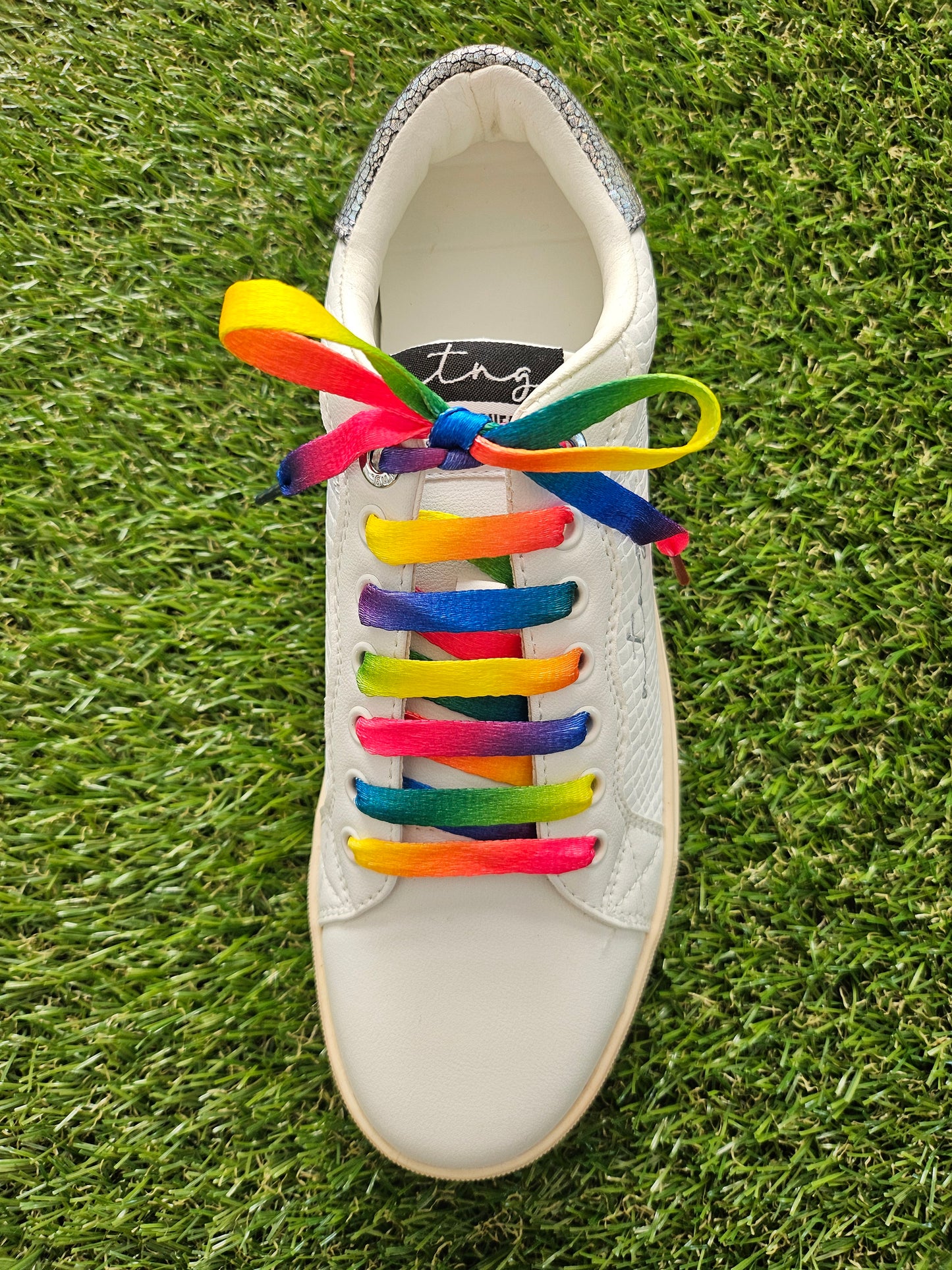 White sneaker with rainbow laces on a grass background