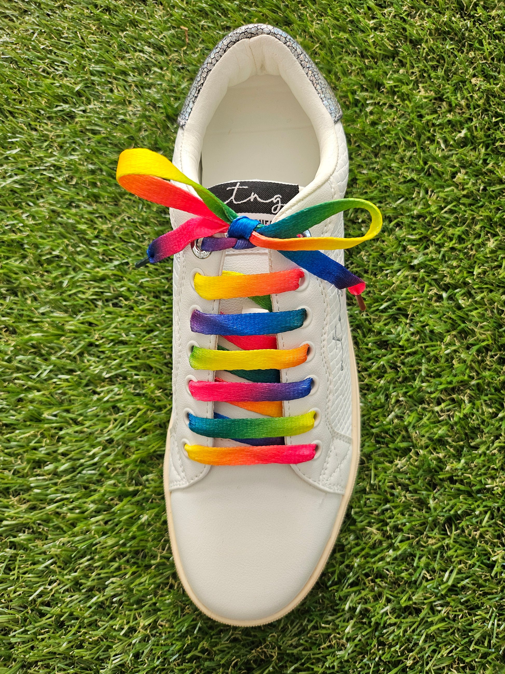 White sneaker with rainbow laces on a grass background