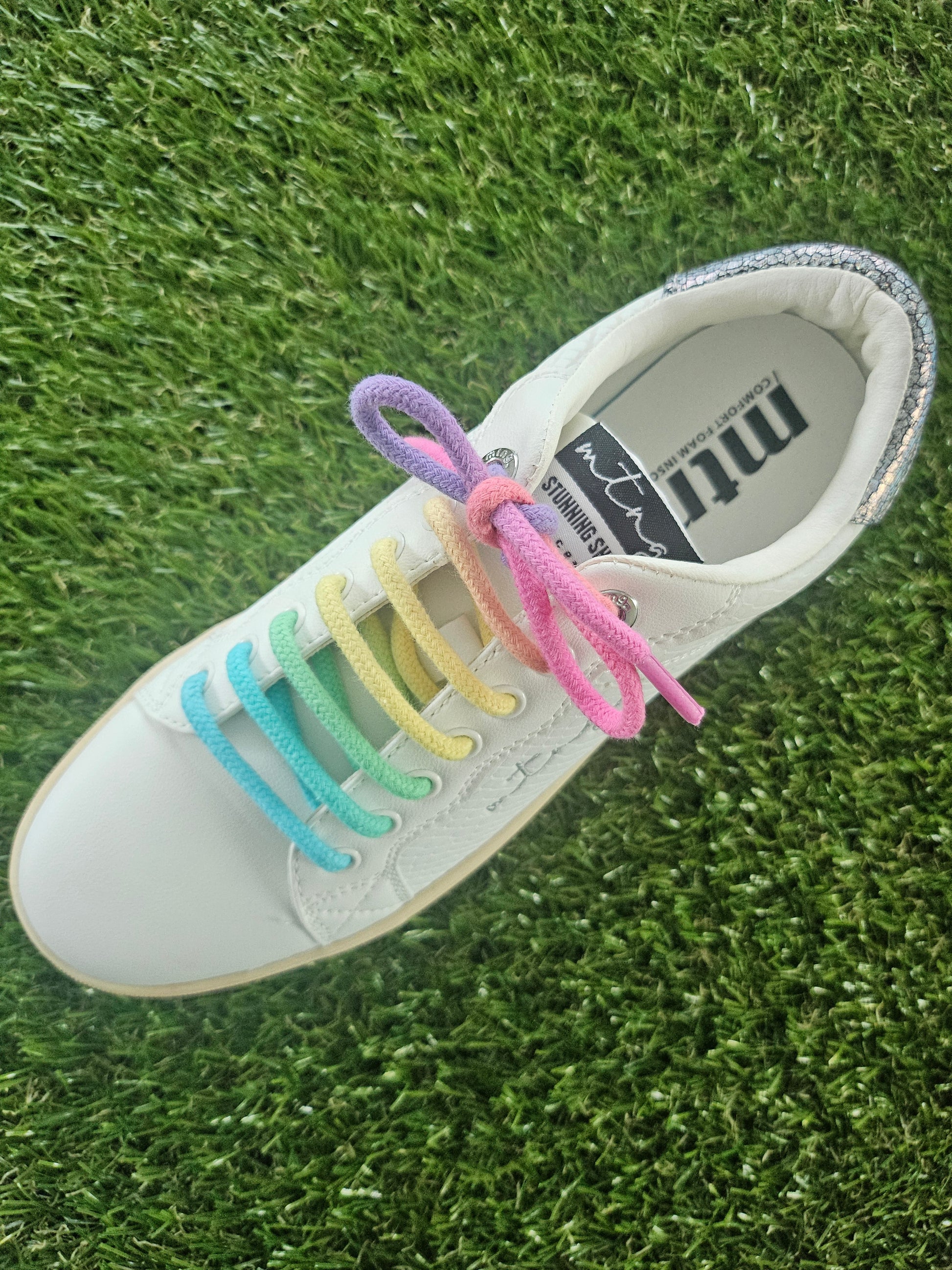 White sneaker with colorful shoelaces on a grass background