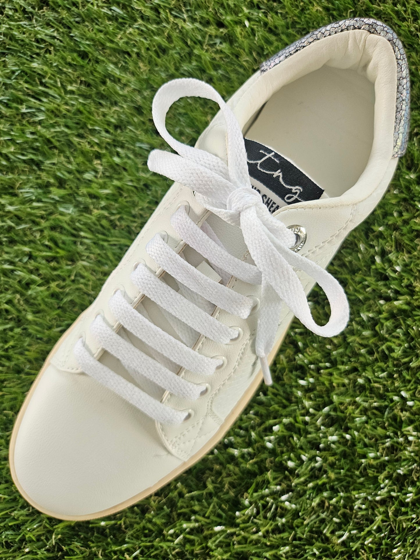 White sneaker with white laces on a grass background