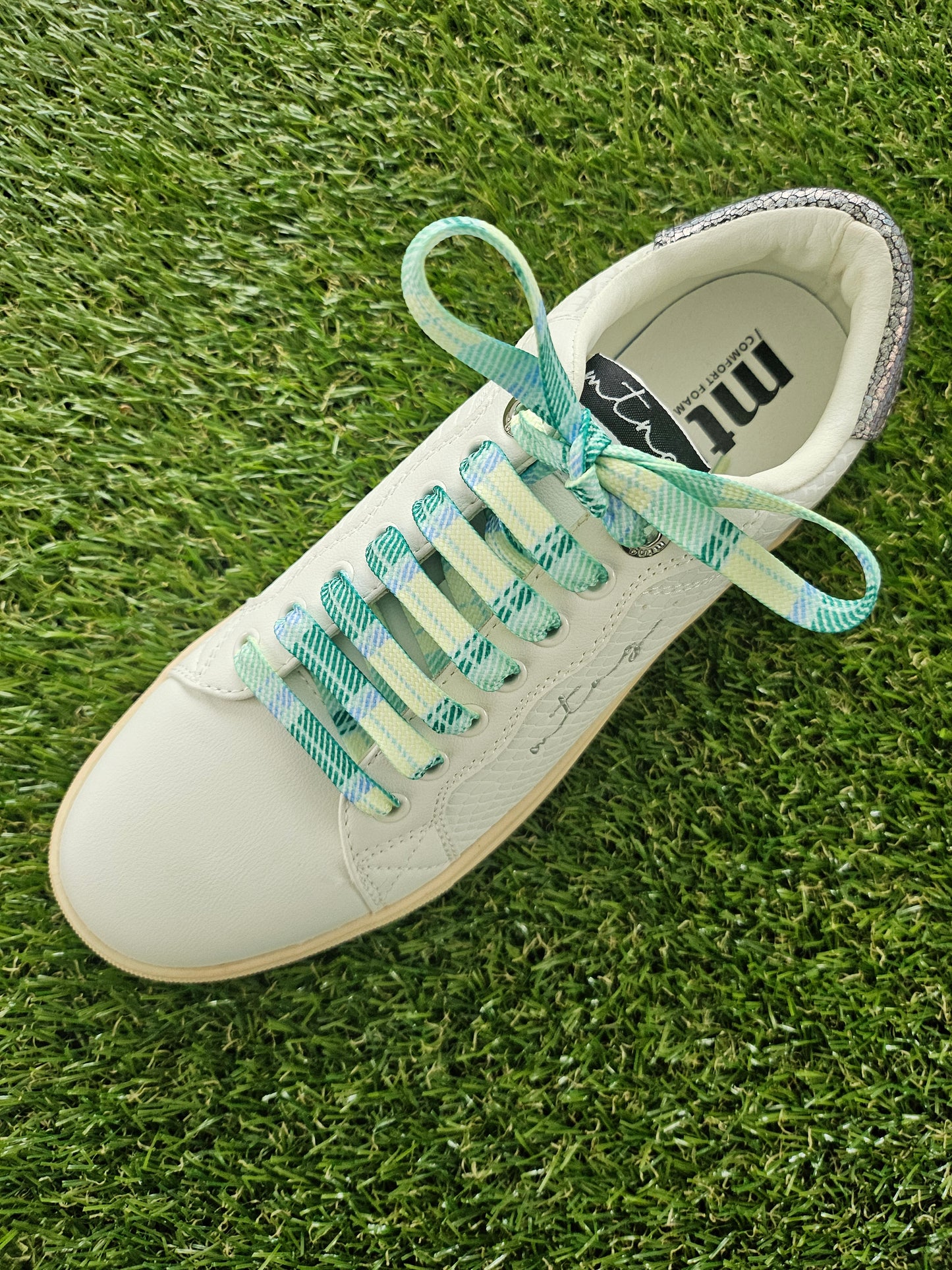 White sneaker with green and blue tartan laces on grass