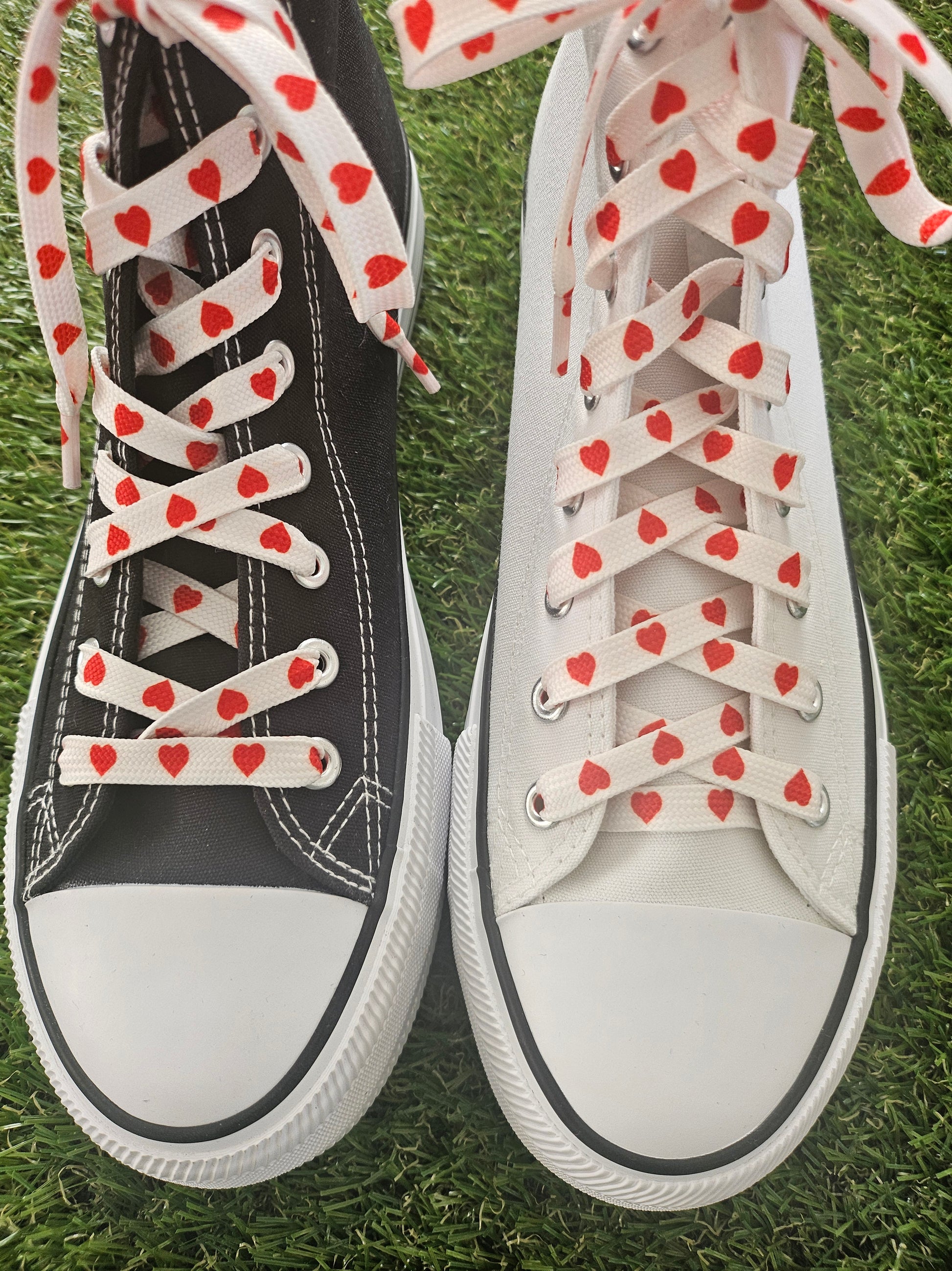 Pair of sneakers with heart-patterned laces on a grass background