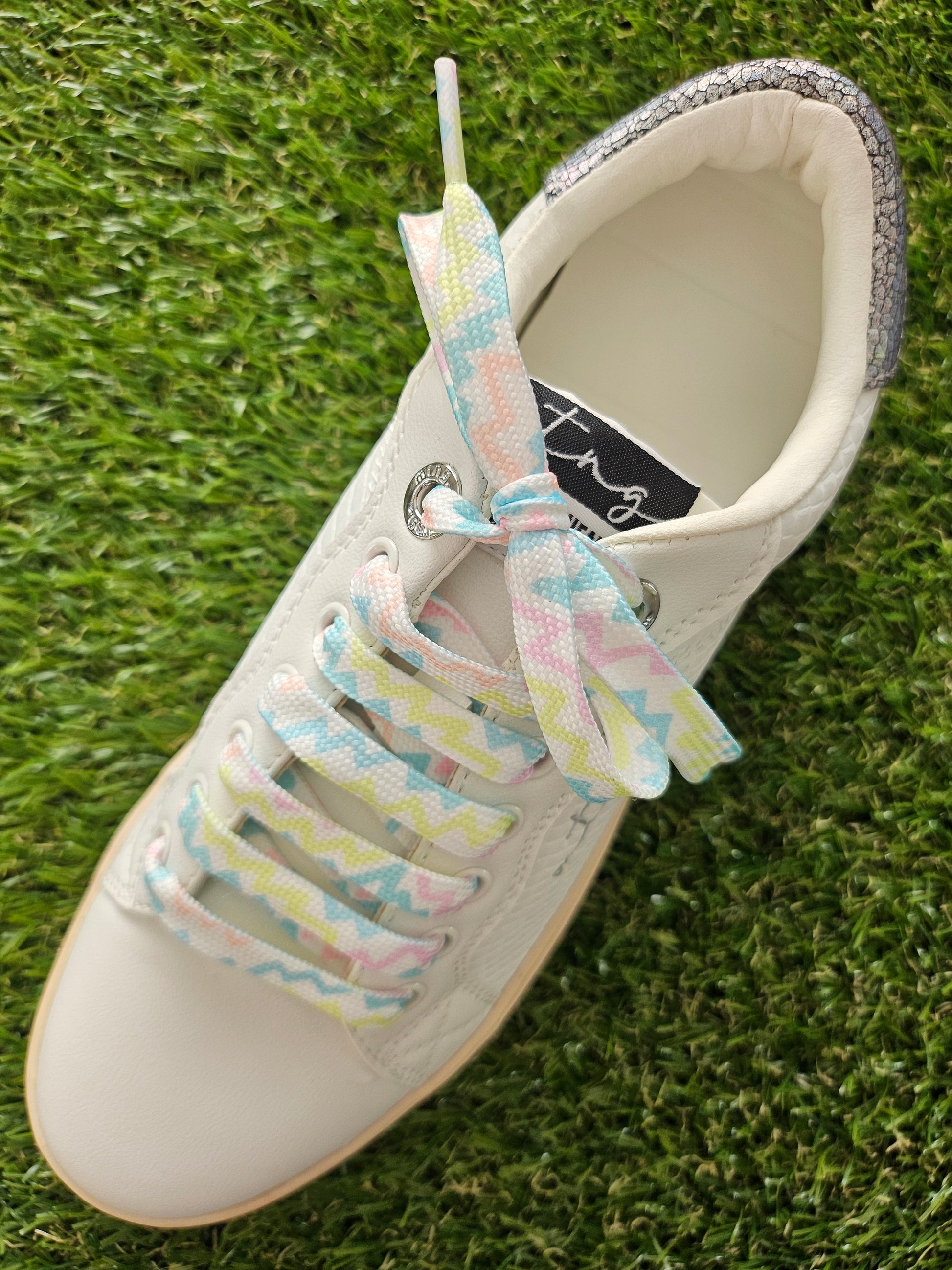 White sneaker with colorful shoelaces on a grass background