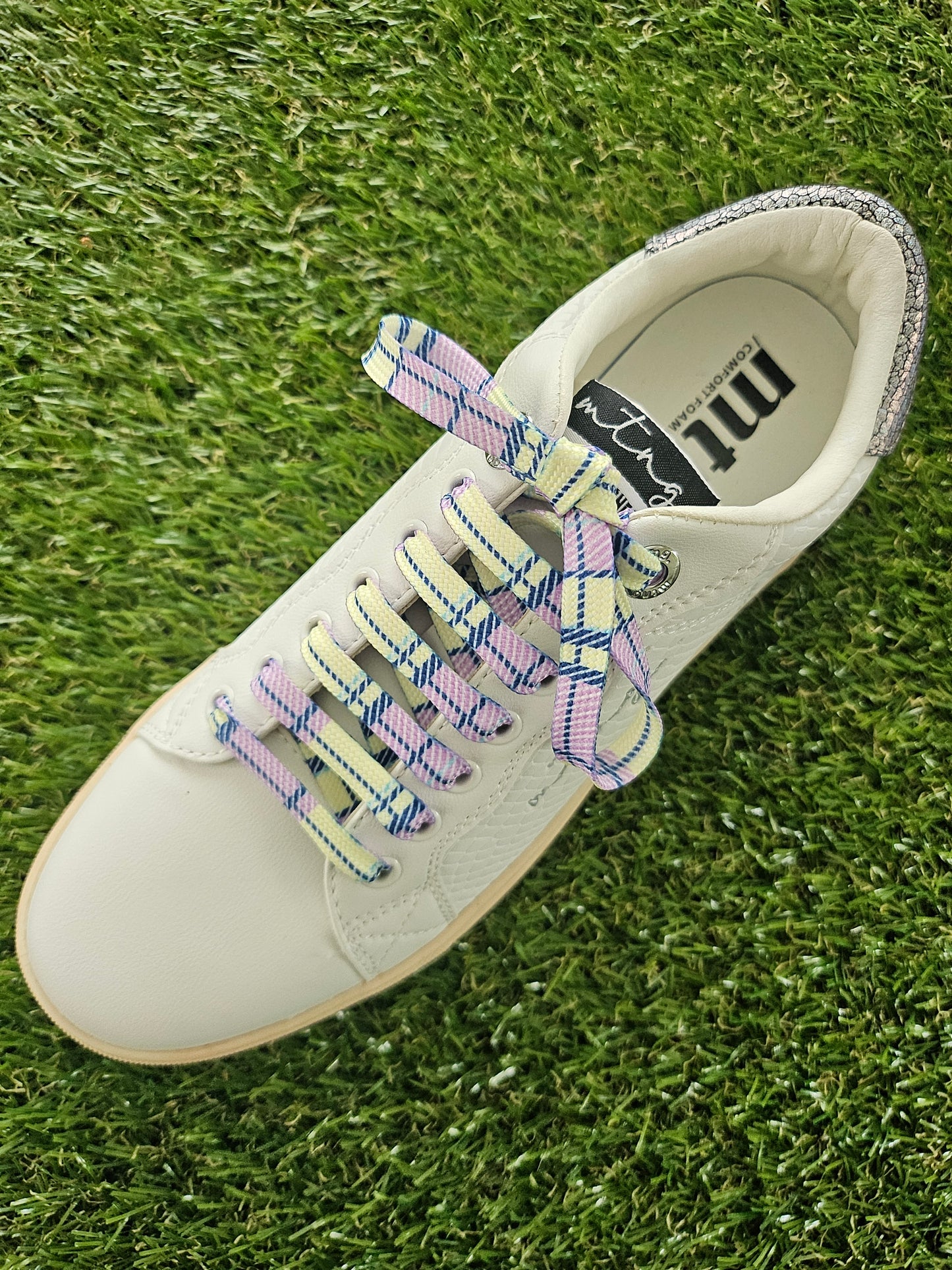 White sneaker with plaid tartan laces on grass