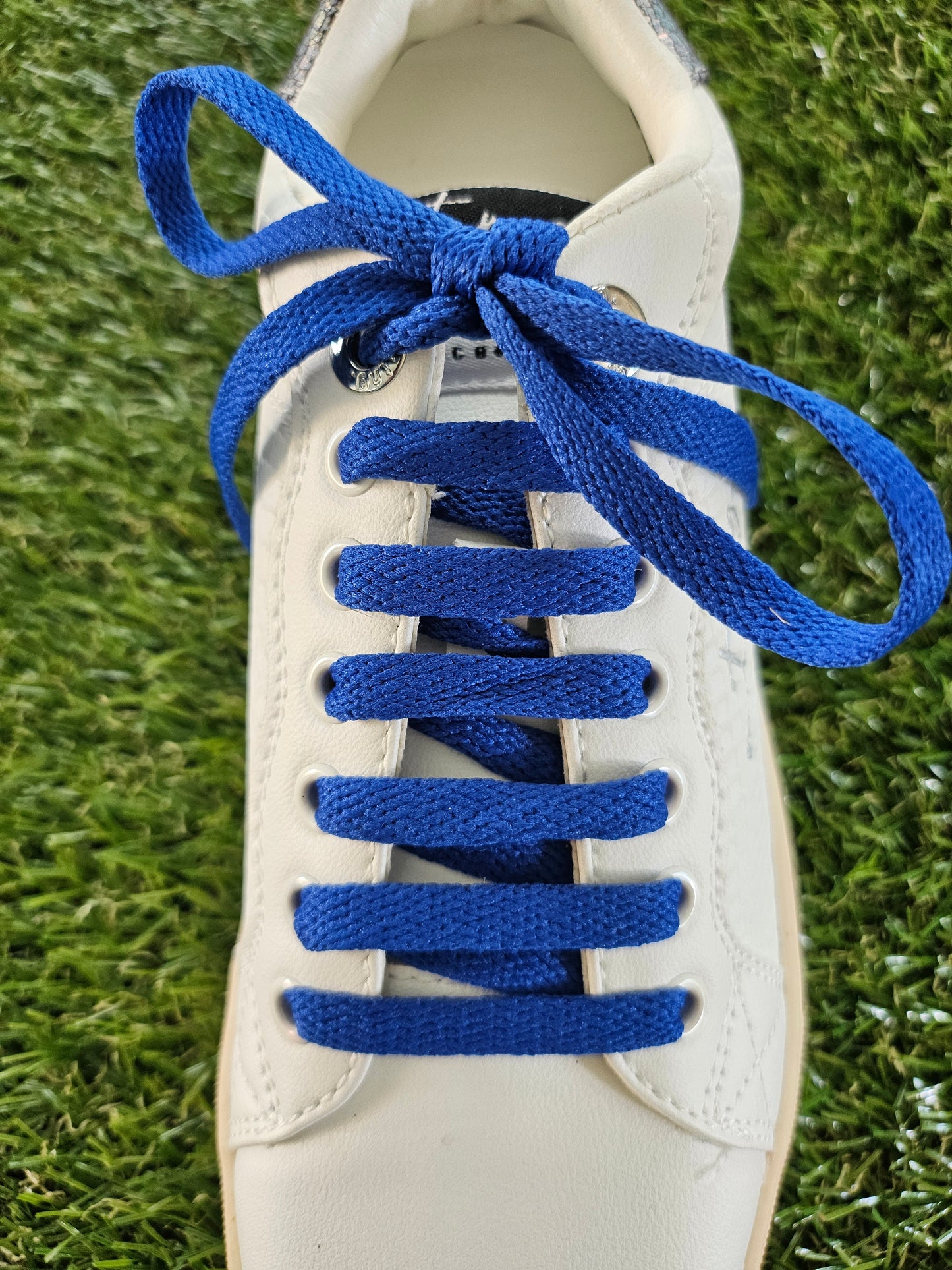White sneaker with blue shoelaces on a grass background