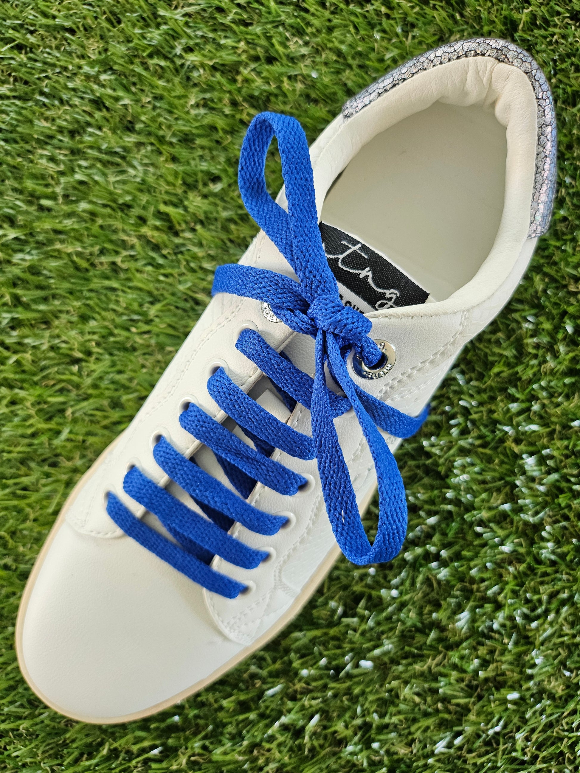 White sneaker with blue laces on a grass background