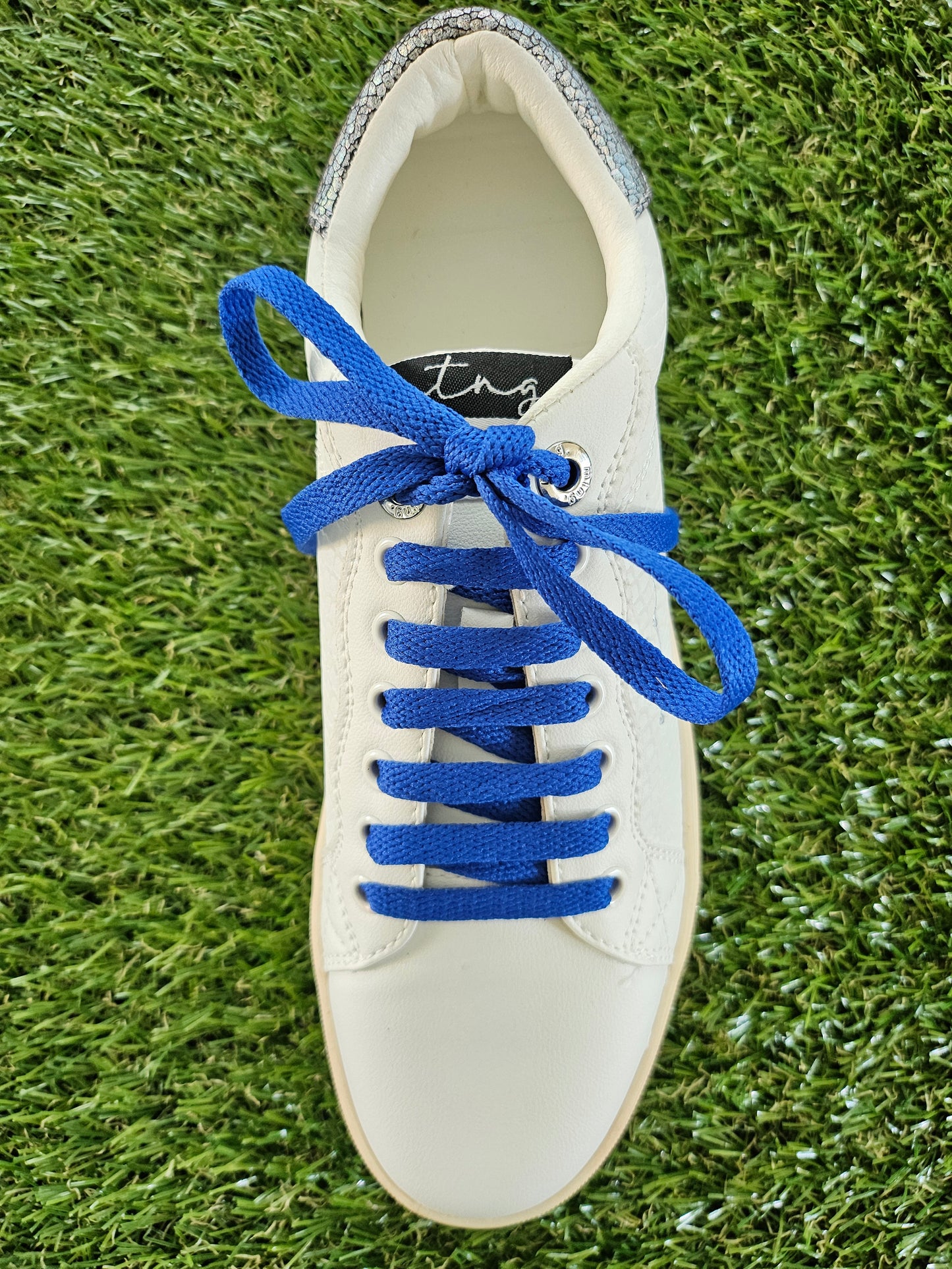 White sneaker with blue laces on a grass background