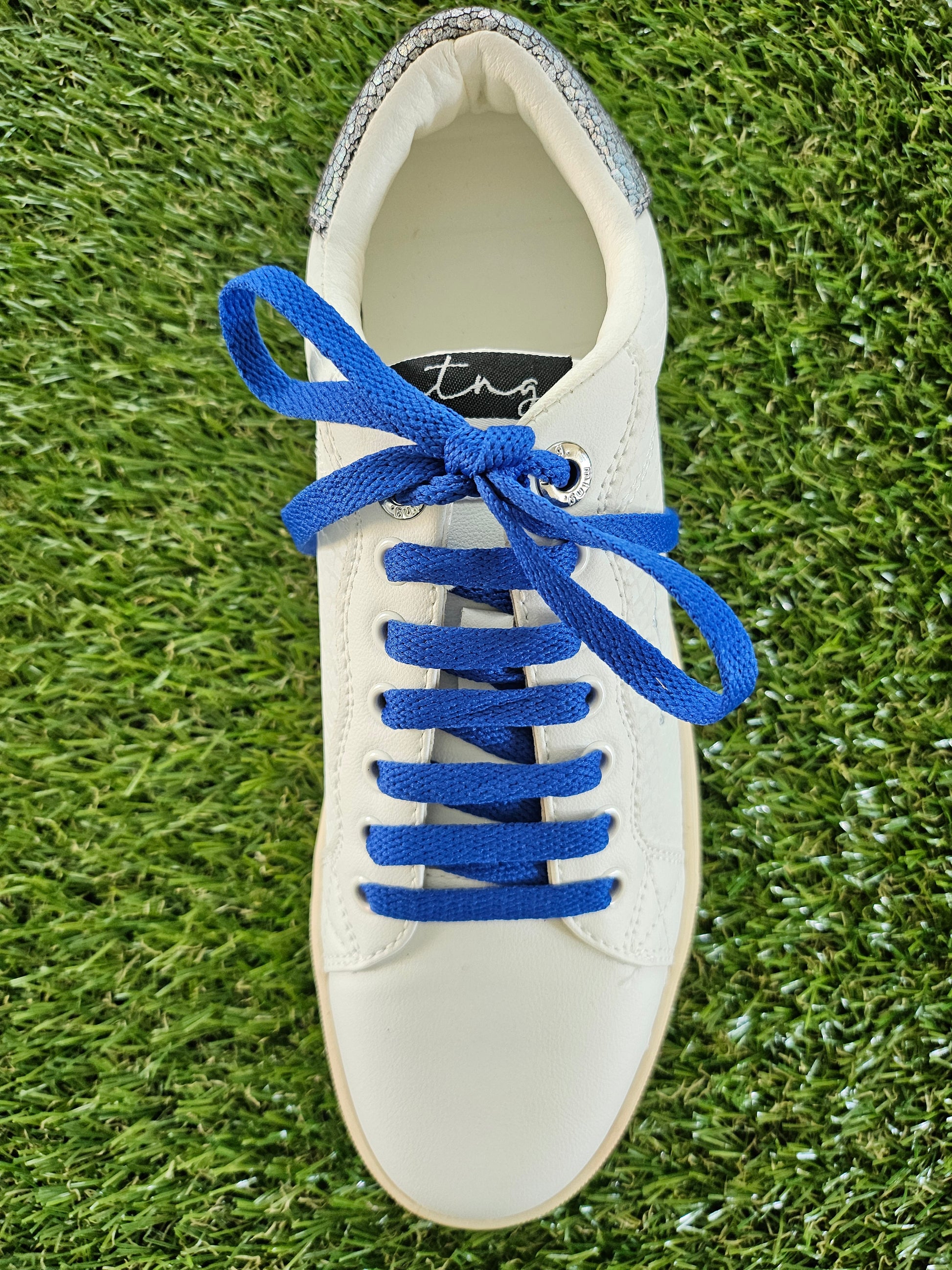 White sneaker with blue laces on a grass background