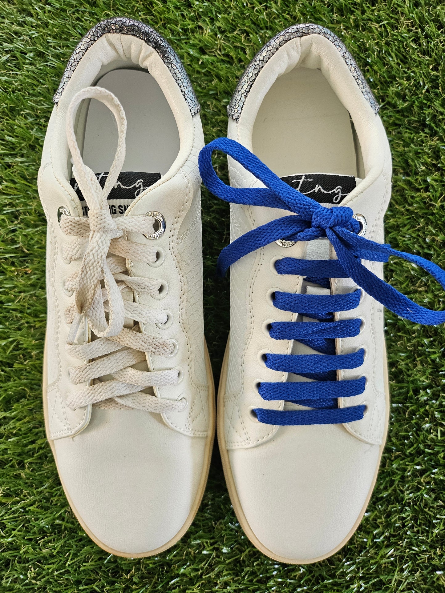 White sneakers with blue and white laces on a grass background