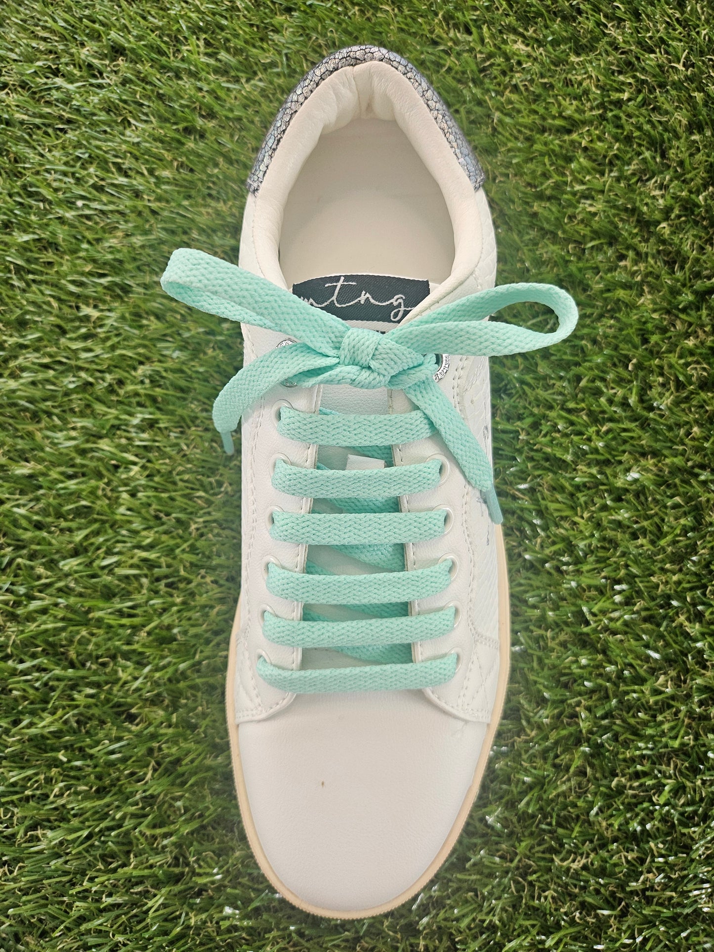 White sneaker with mint green laces on grass