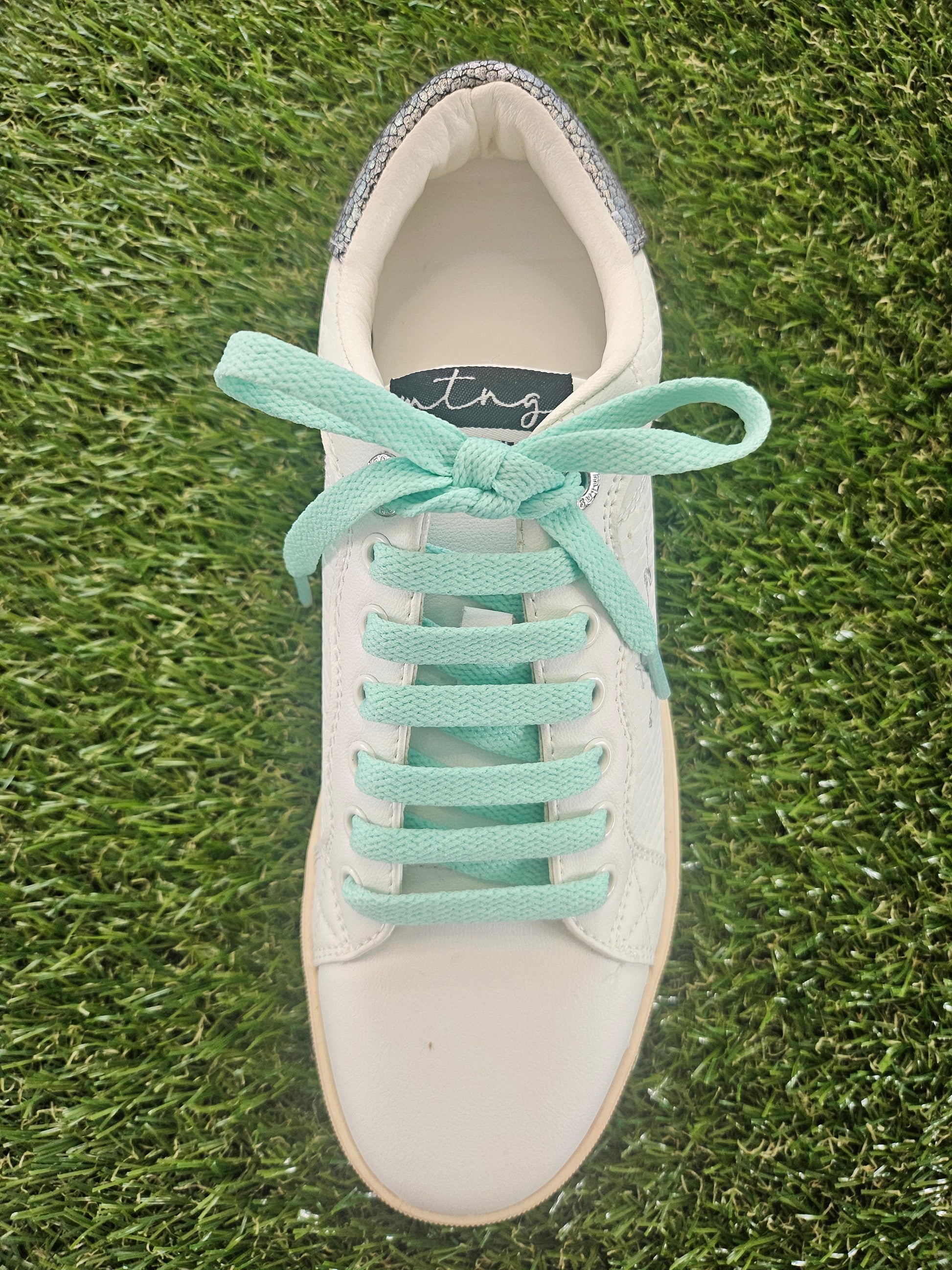White sneaker with mint green laces on grass