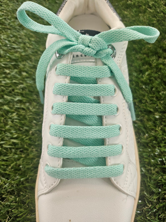White sneaker with mint green shoelaces on a grass background