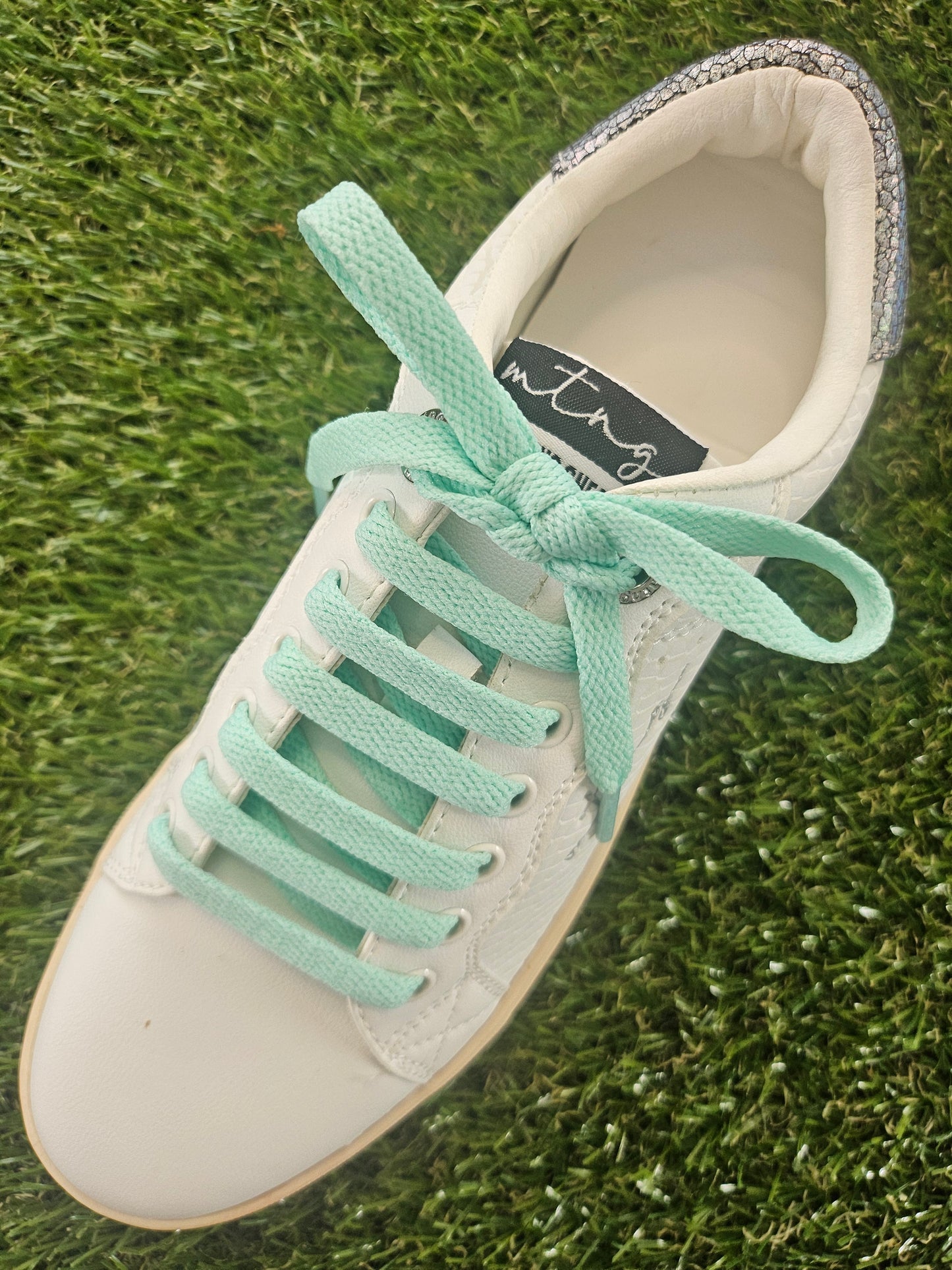 White sneaker with mint green laces on grass