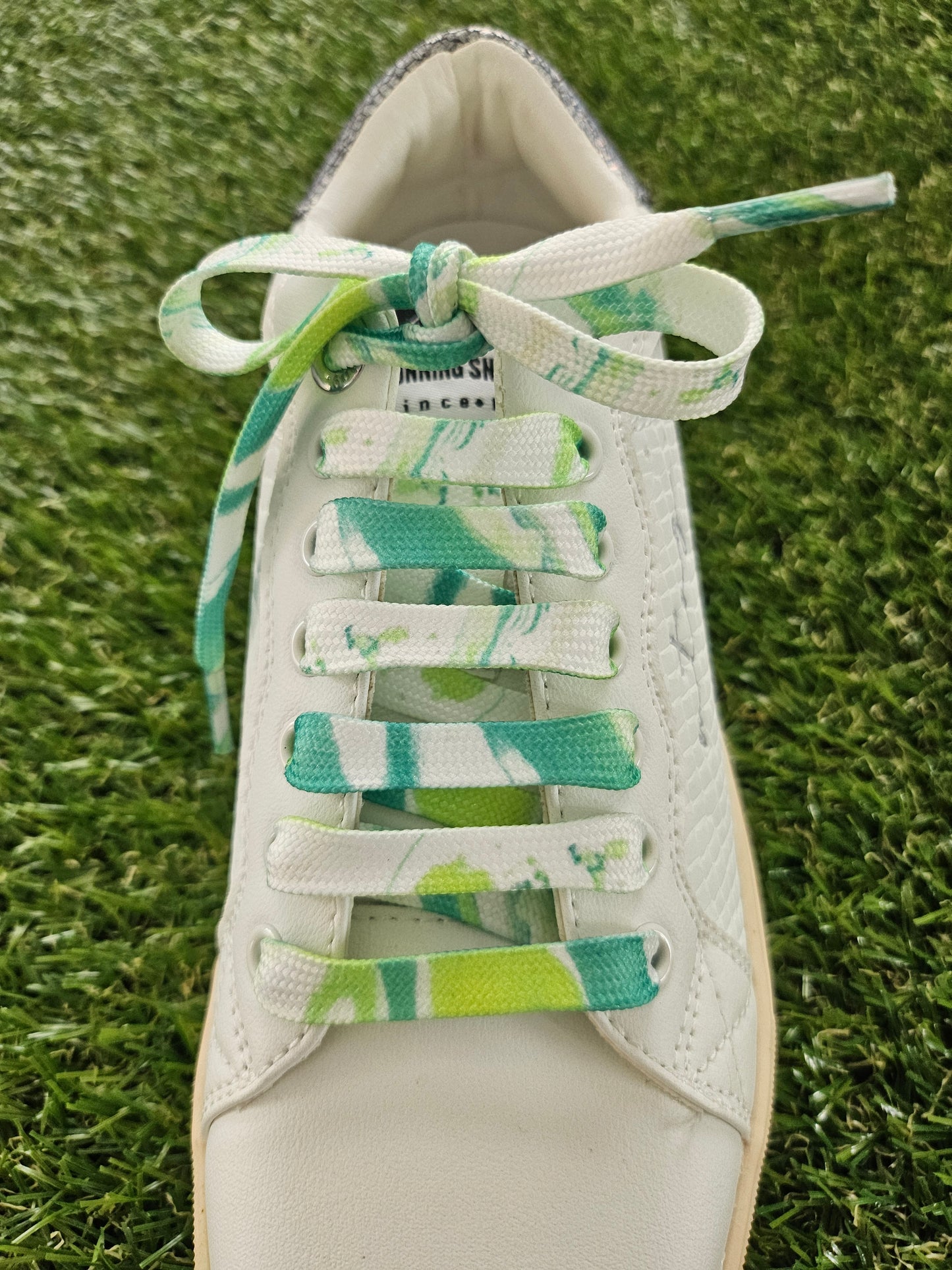 White sneaker with green and white laces on a grass background