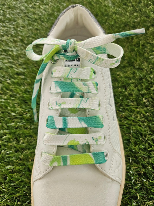 White sneaker with green and white laces on a grass background