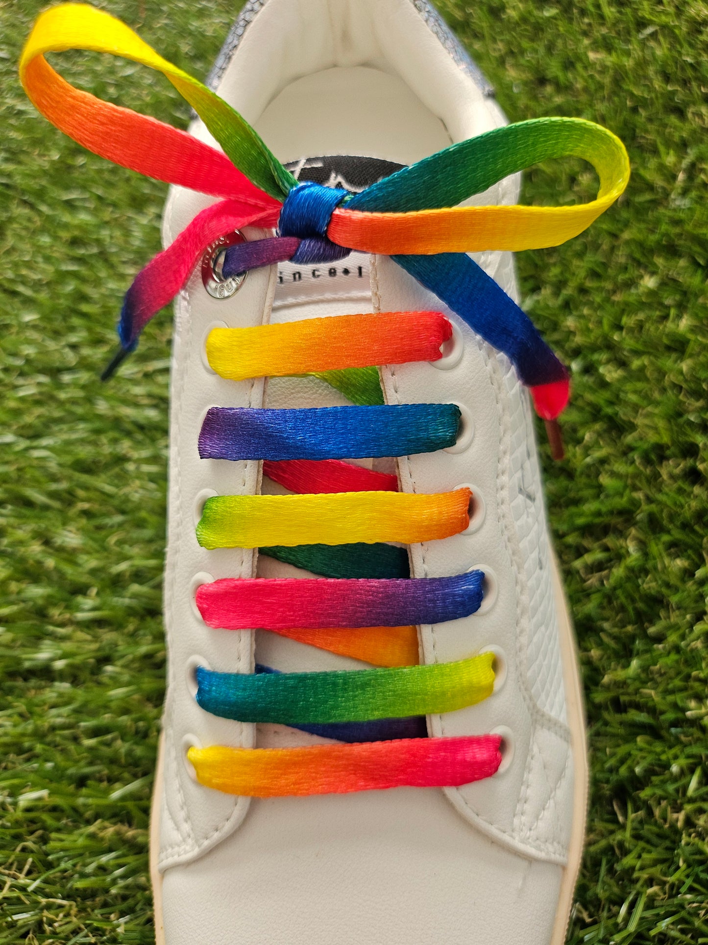 Colorful rainbow shoelaces on a white sneaker with grass background