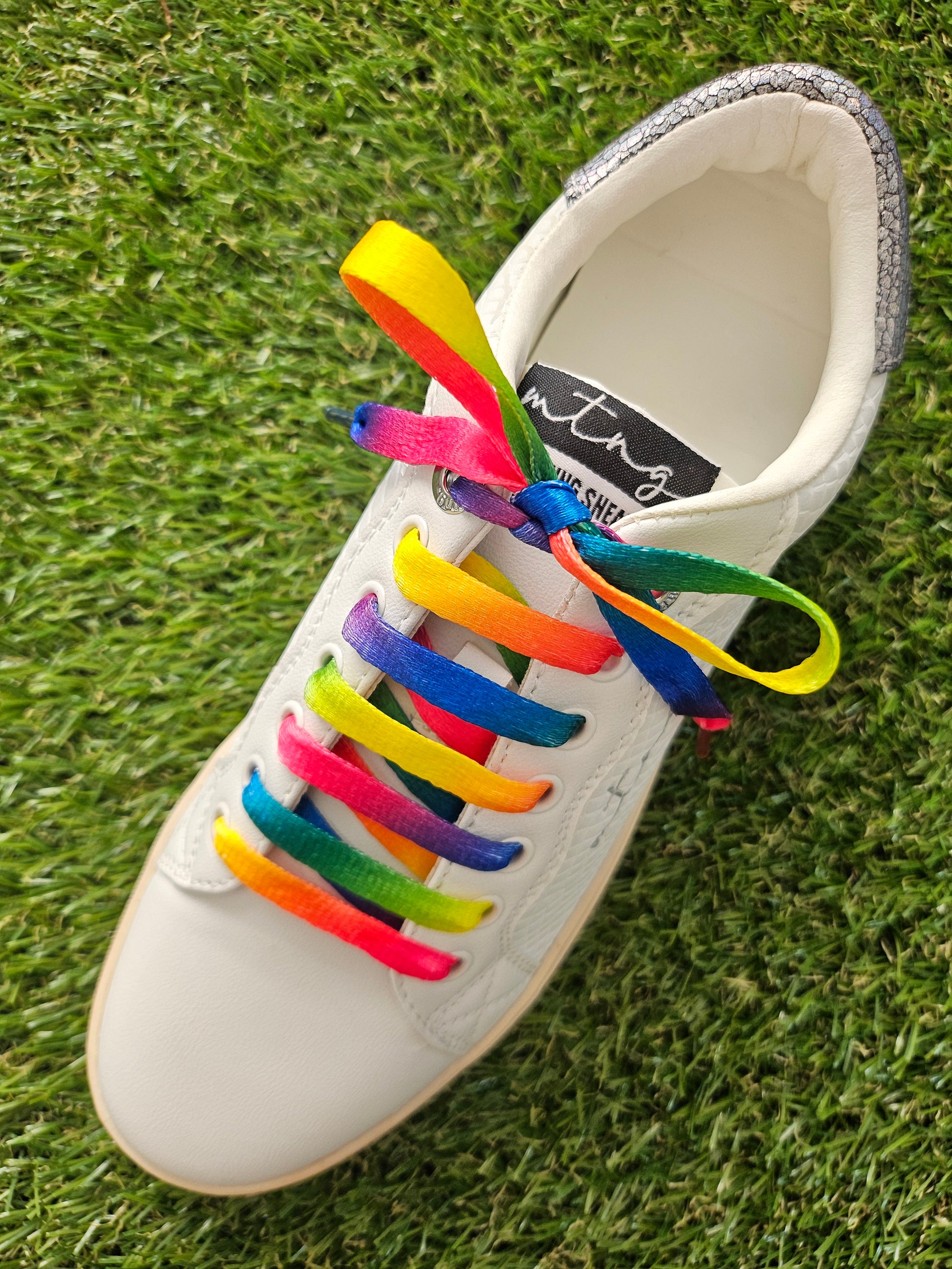 White shoe with colorful rainbow patterned shoelaces on a grass background
