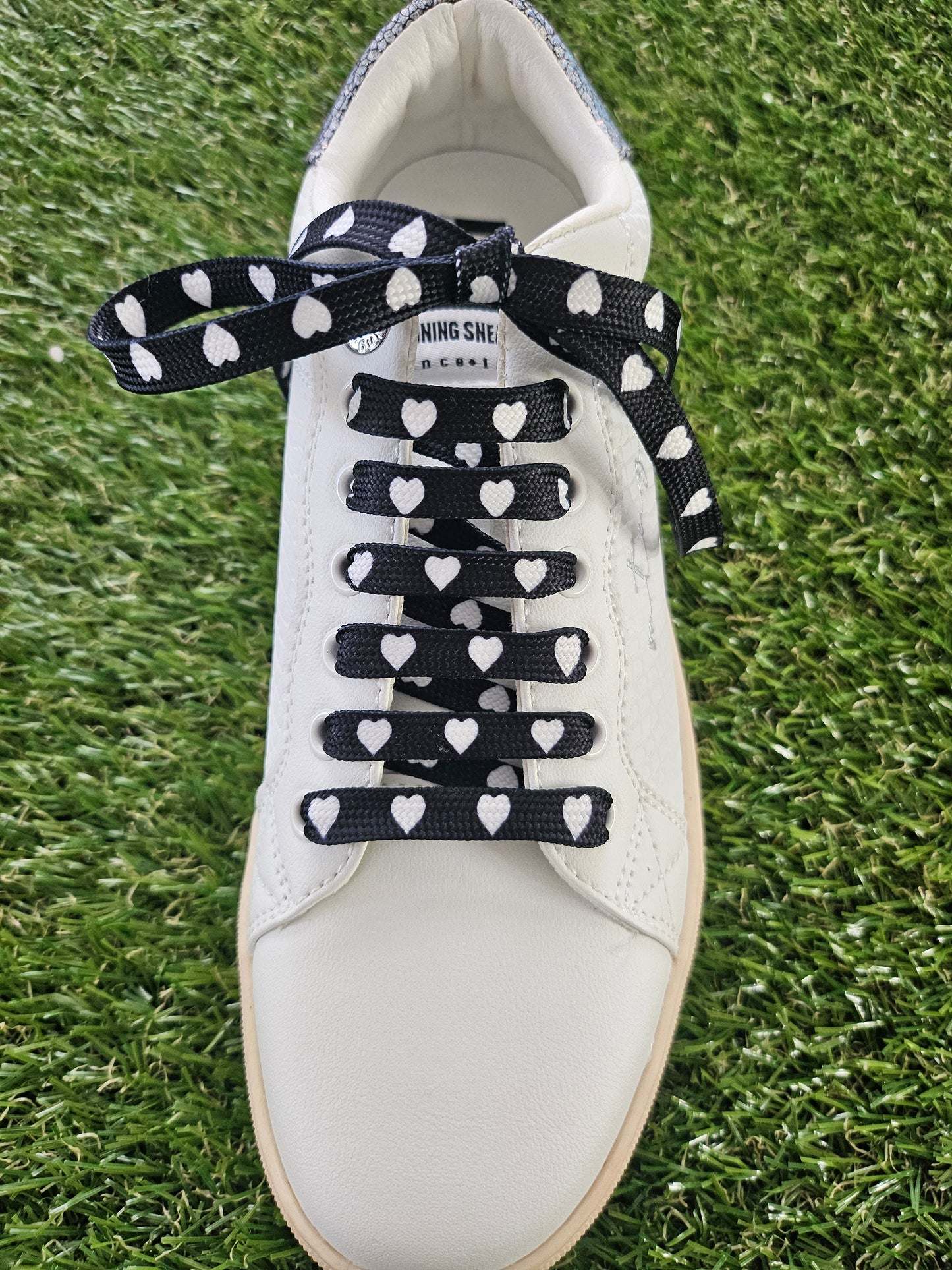 white trainer with white love hearts on black shoelaces on a grass