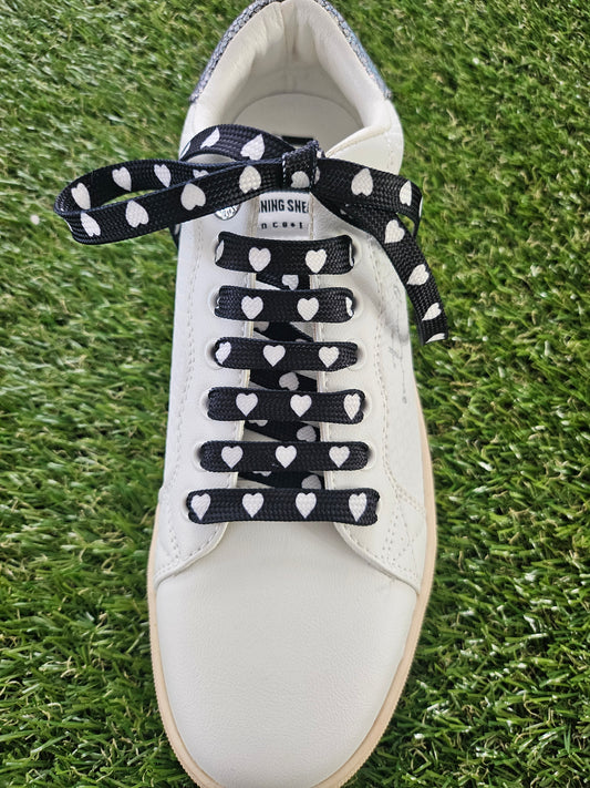 white trainer with white love hearts on black shoelaces on a grass