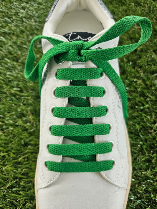 White sneaker with green laces on a grass background