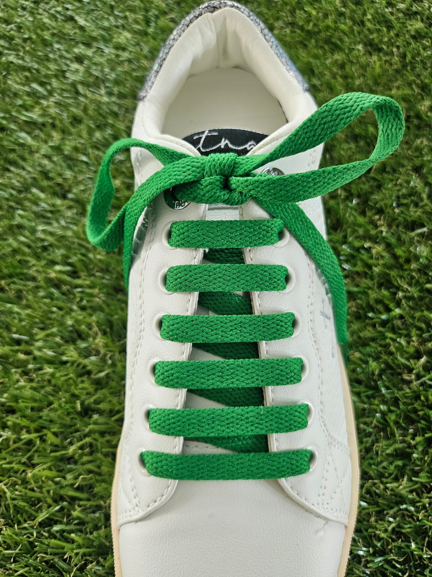 White sneaker with green laces on a grass background