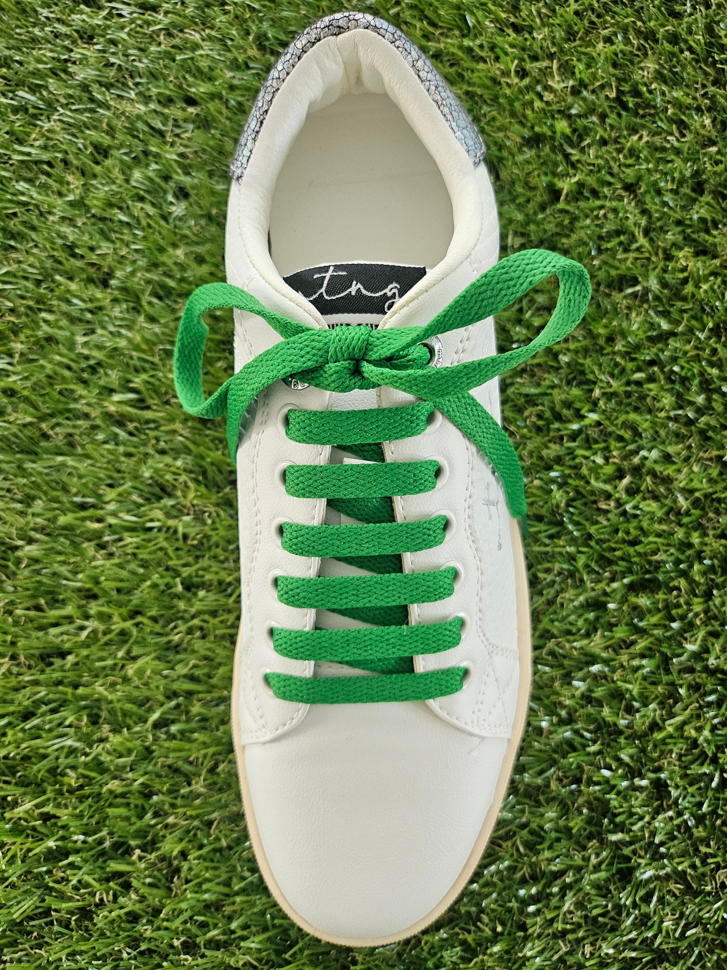 White sneaker with green laces on grass