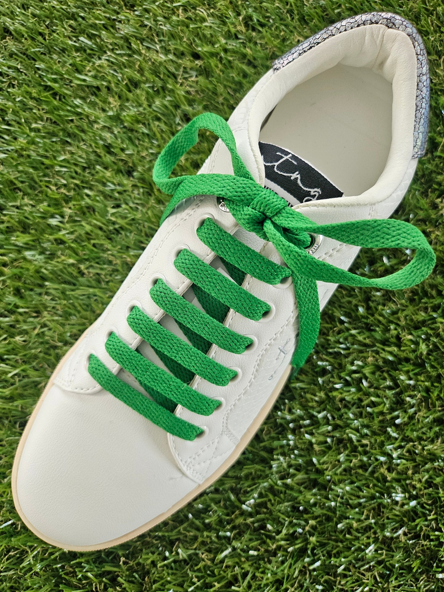 White sneaker with green laces on grass