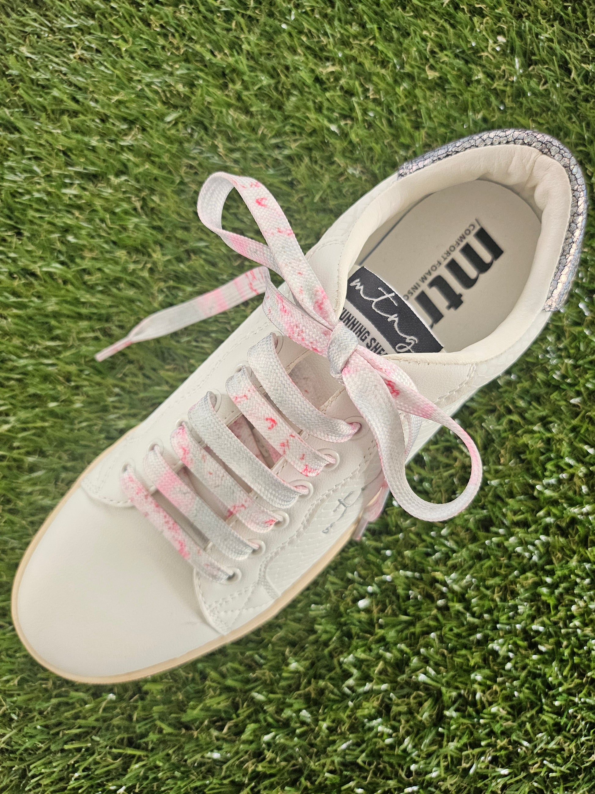 White sneaker with pink laces on grass