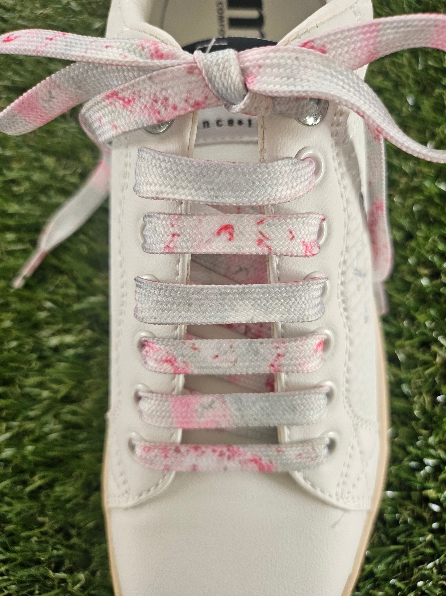 White sneaker with pink speckled laces on a grass background