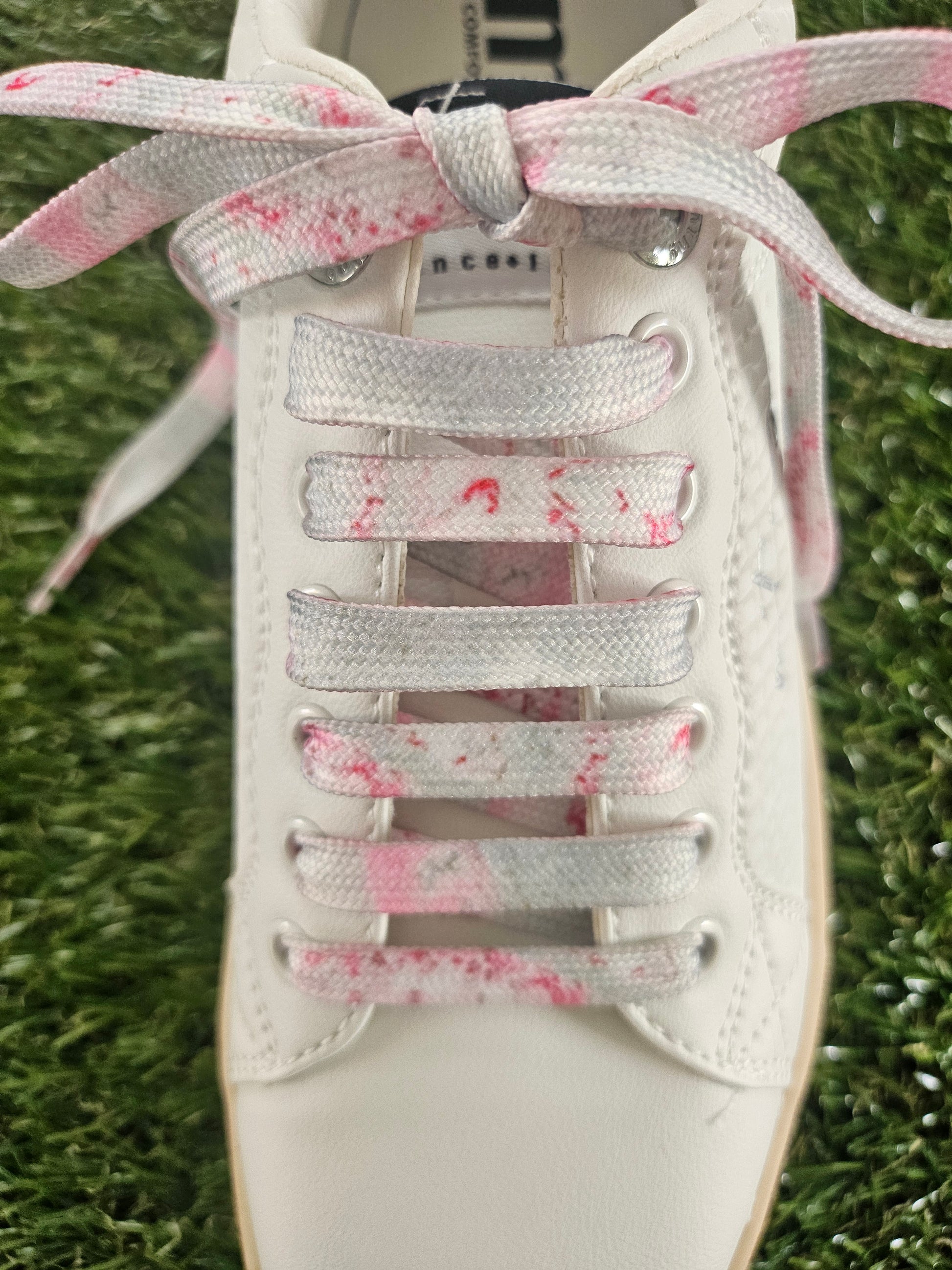 White sneaker with pink speckled laces on a grass background