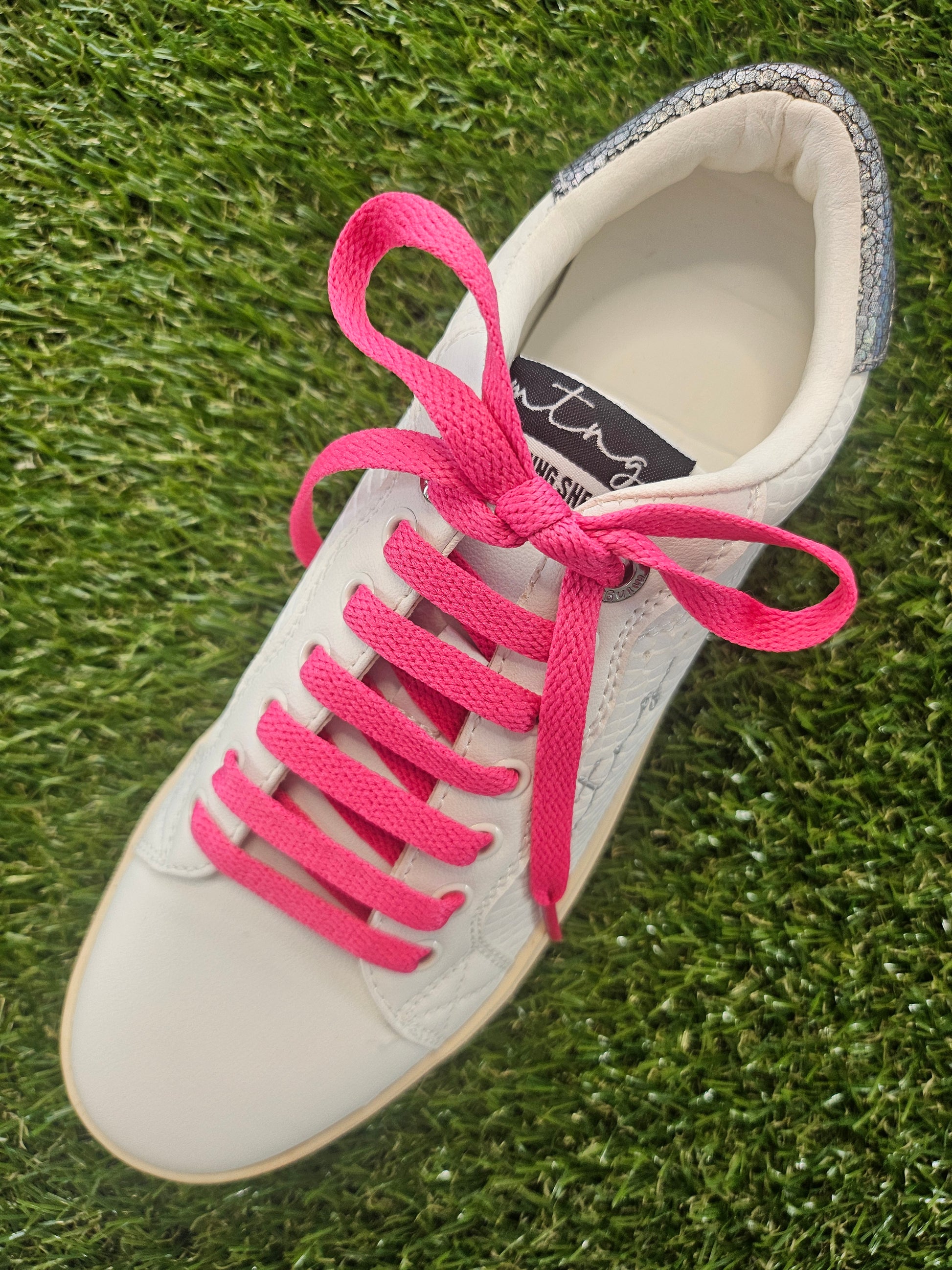 White sneaker with pink laces on grass