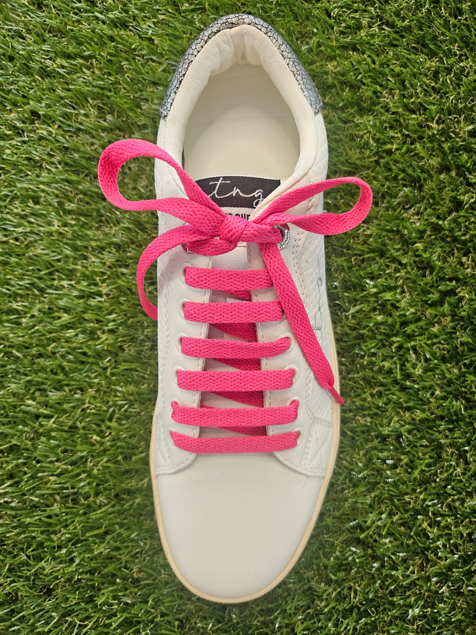 White sneaker with pink laces on a grass background