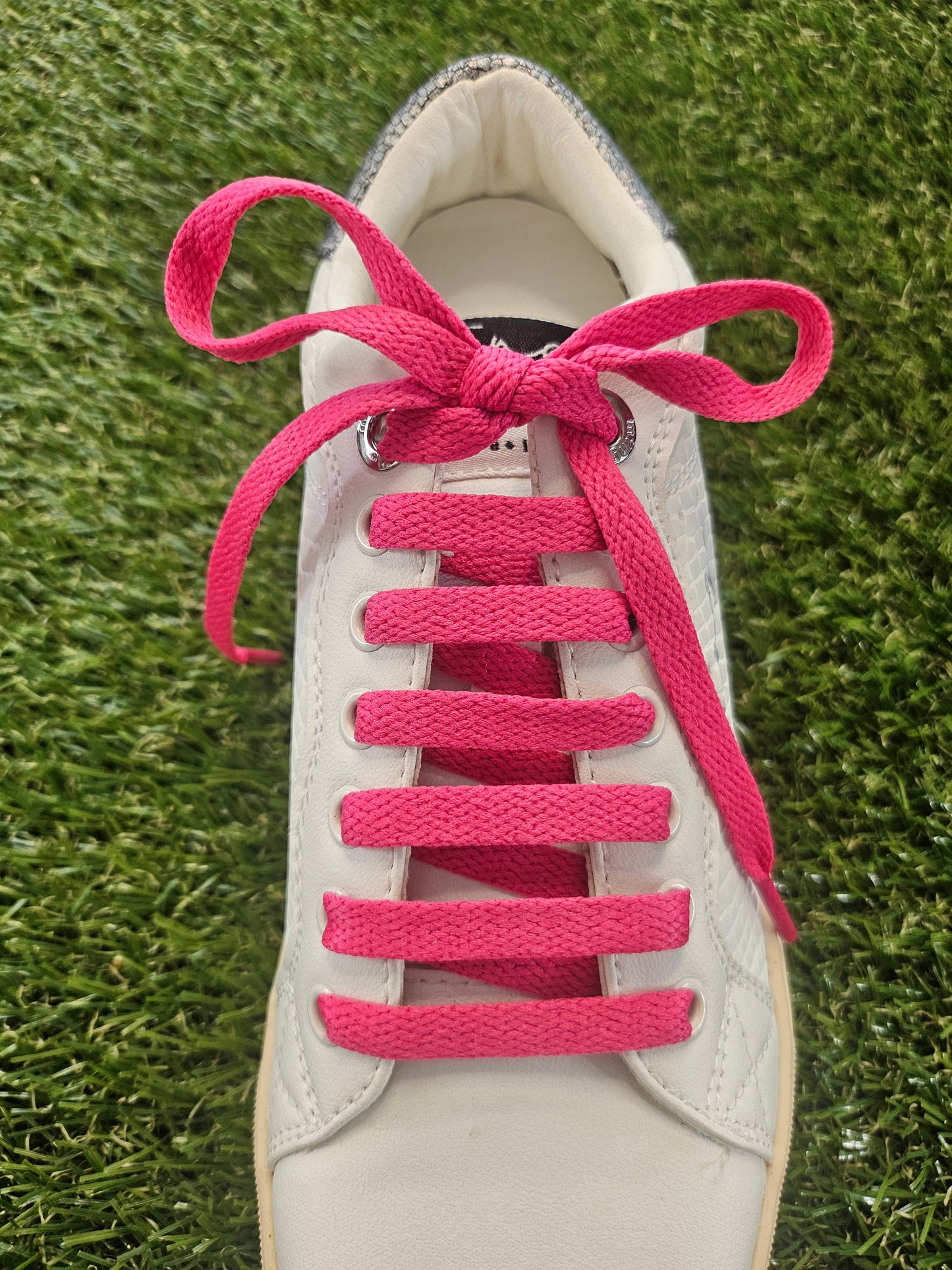 White sneaker with pink laces on a grass background