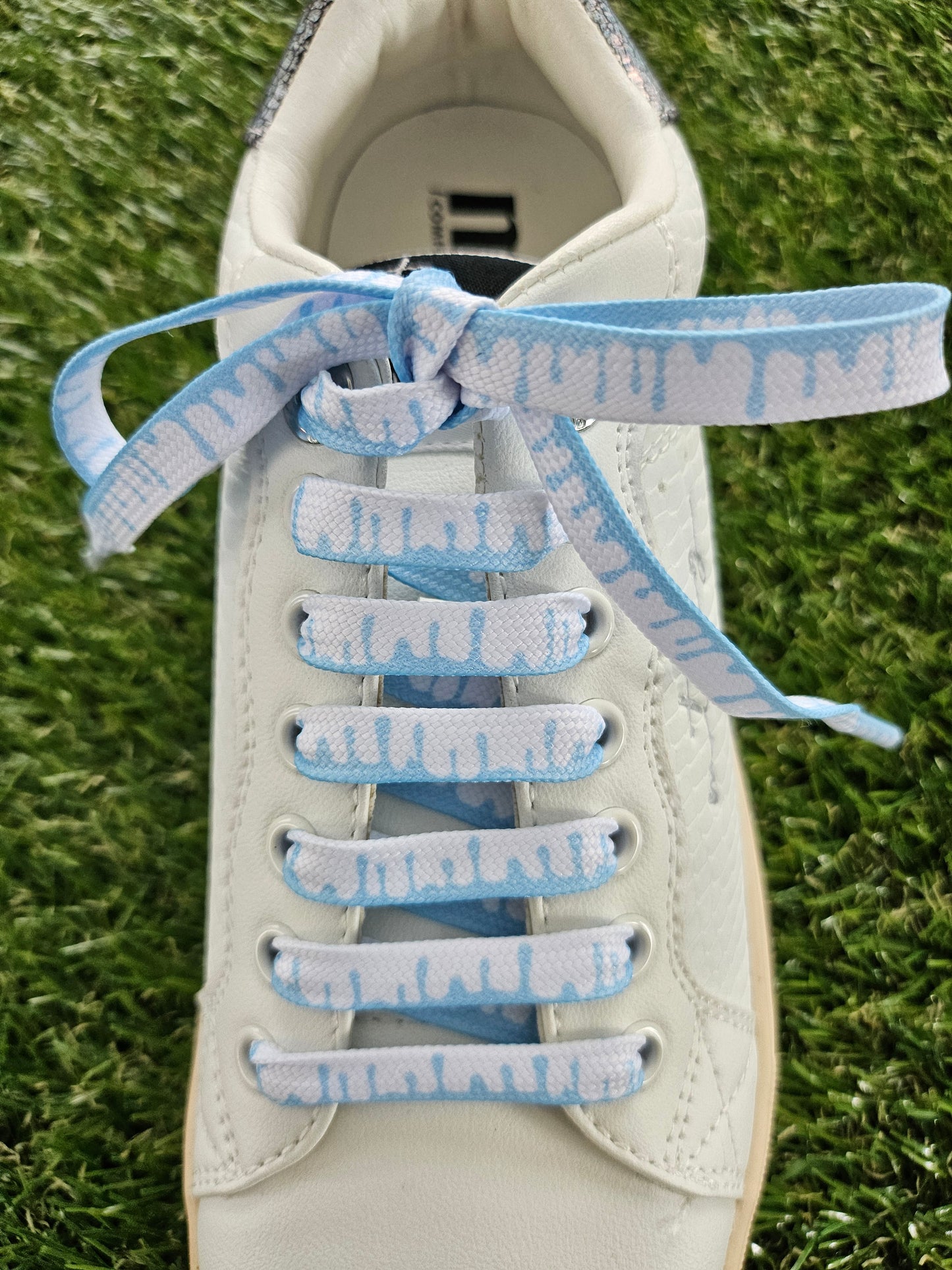 White sneaker with ice blue and white laces on a grass background