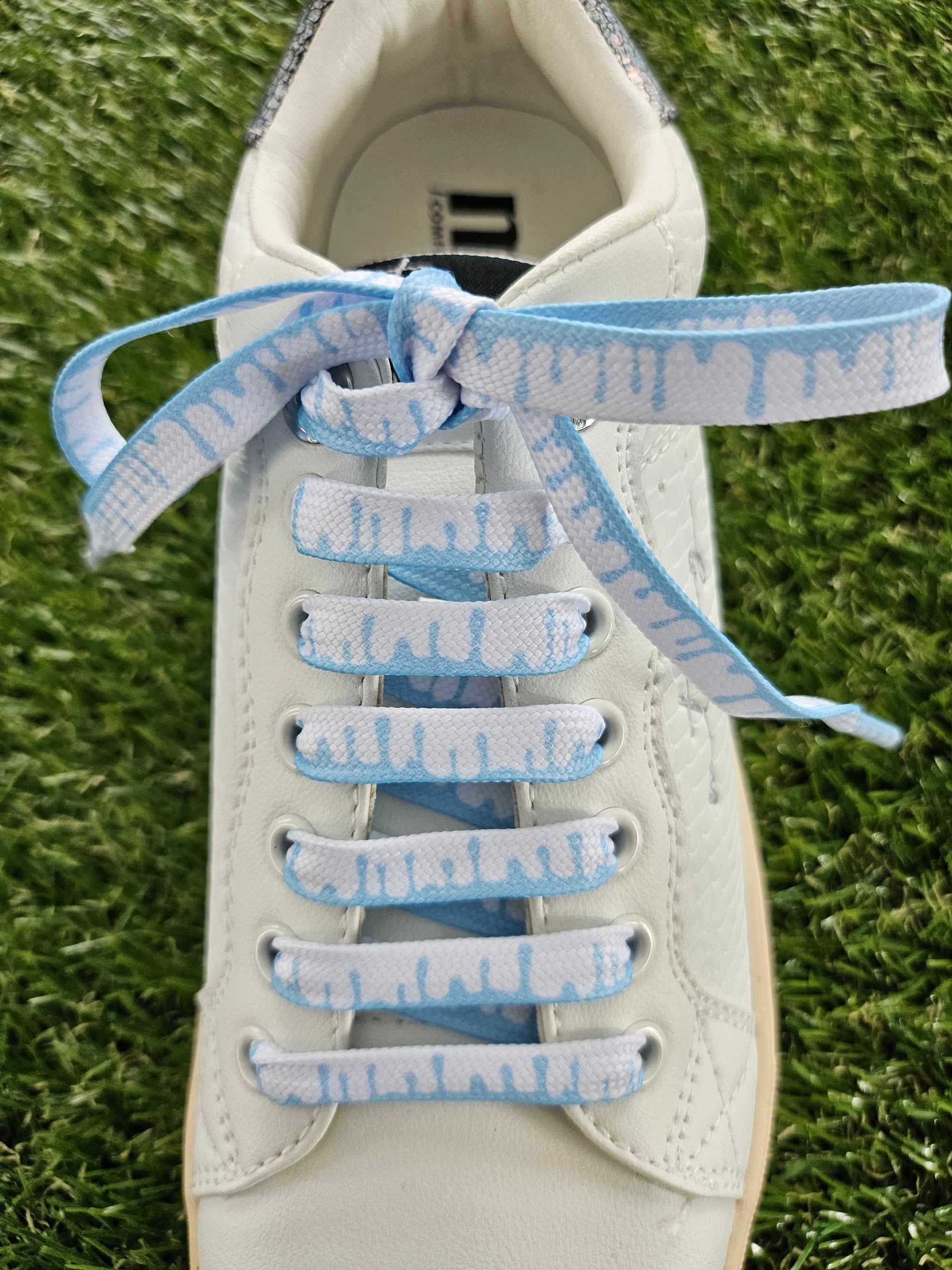 White sneaker with ice blue and white laces on a grass background