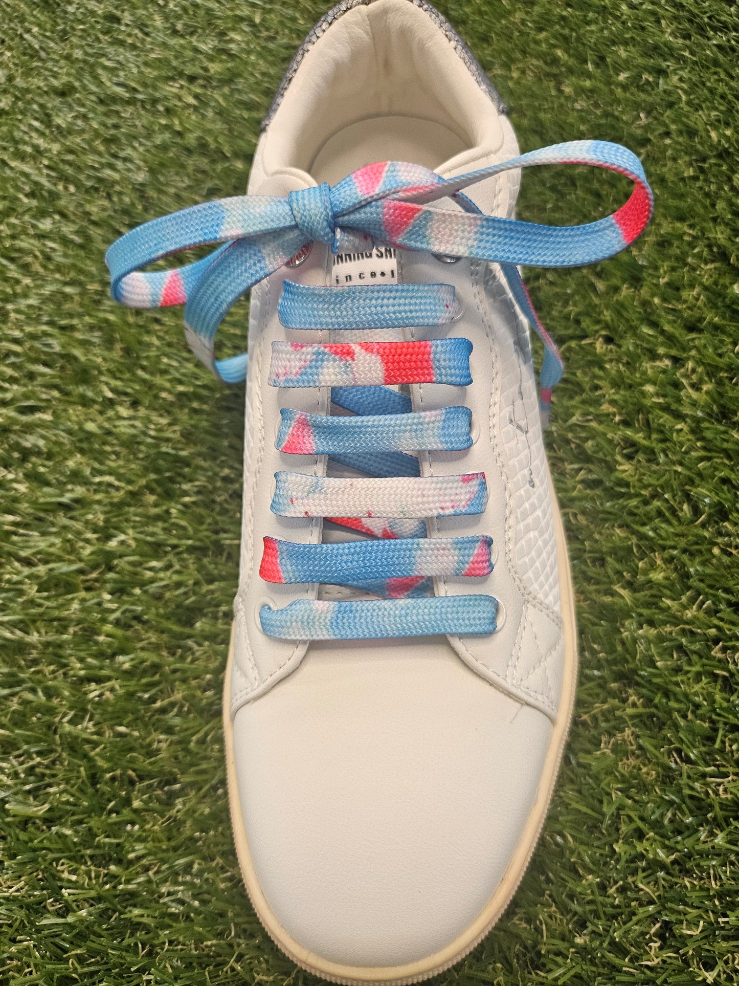White sneaker with colourful laces on a grass background