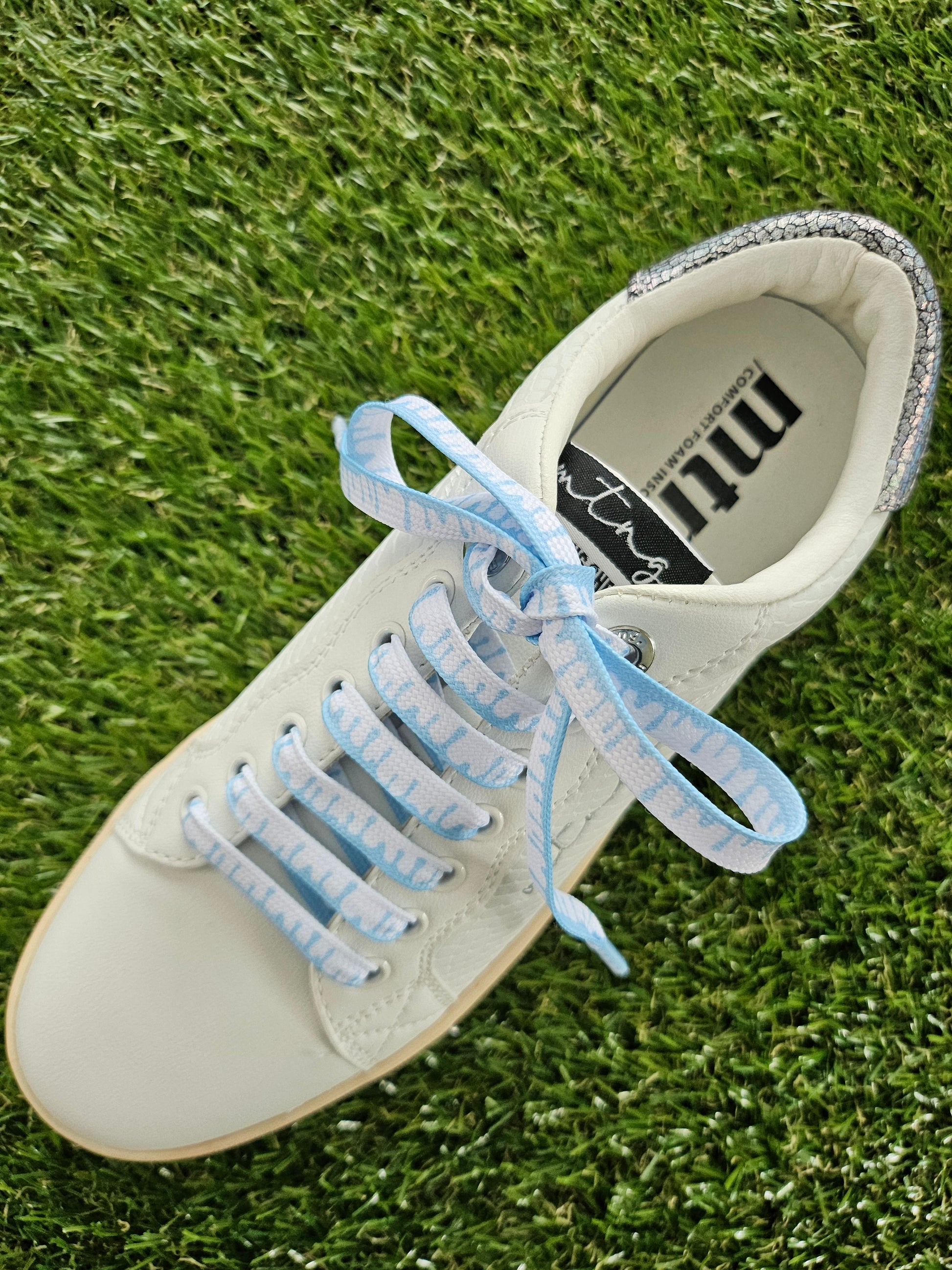 White sneaker with blue laces on grass