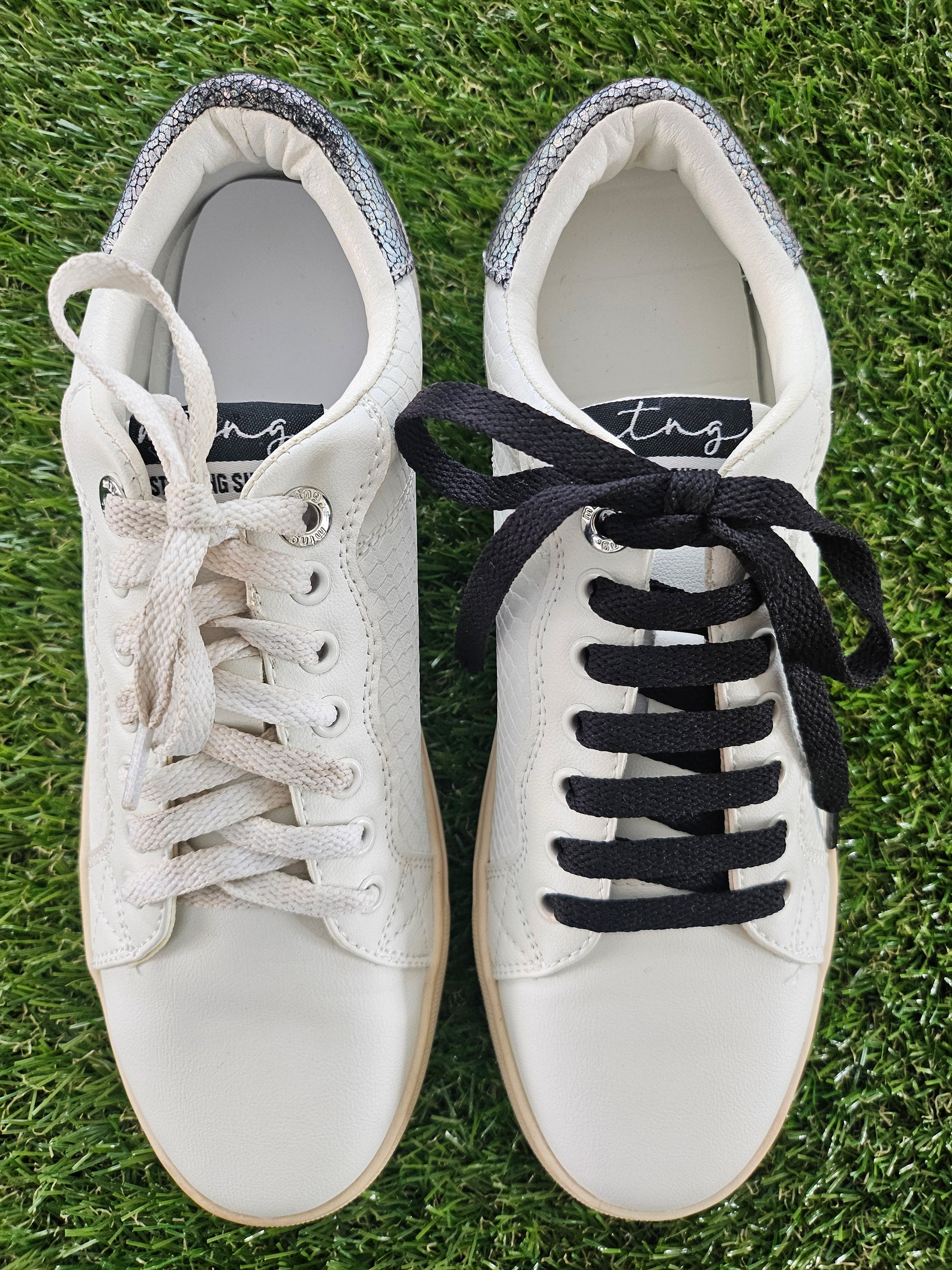 Pair of white sneakers with black laces on a grass background