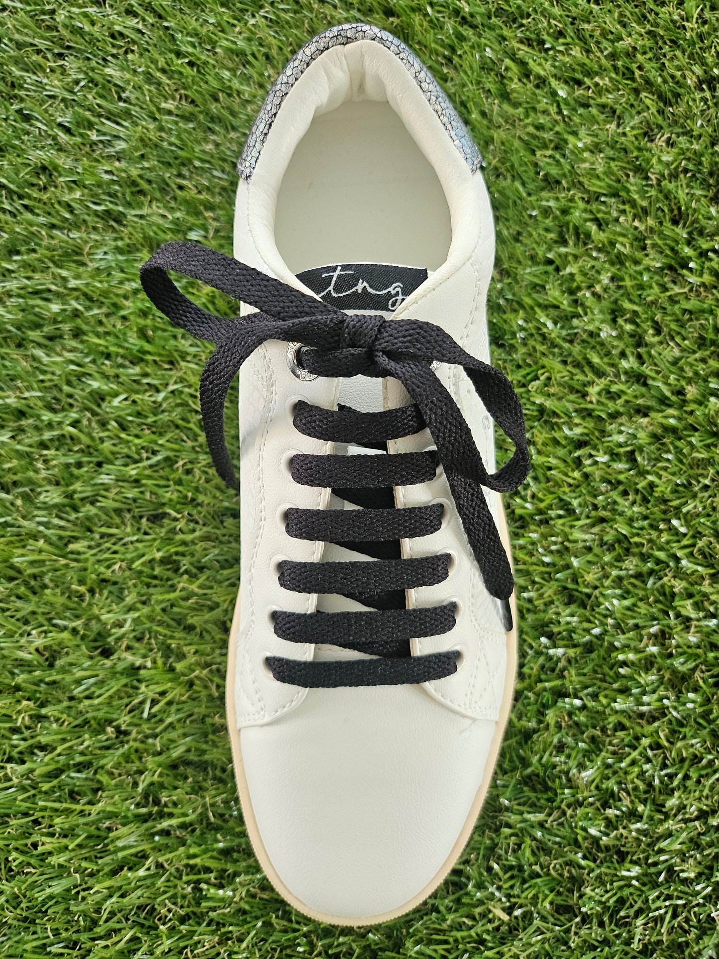 White sneaker with black laces on a grass background
