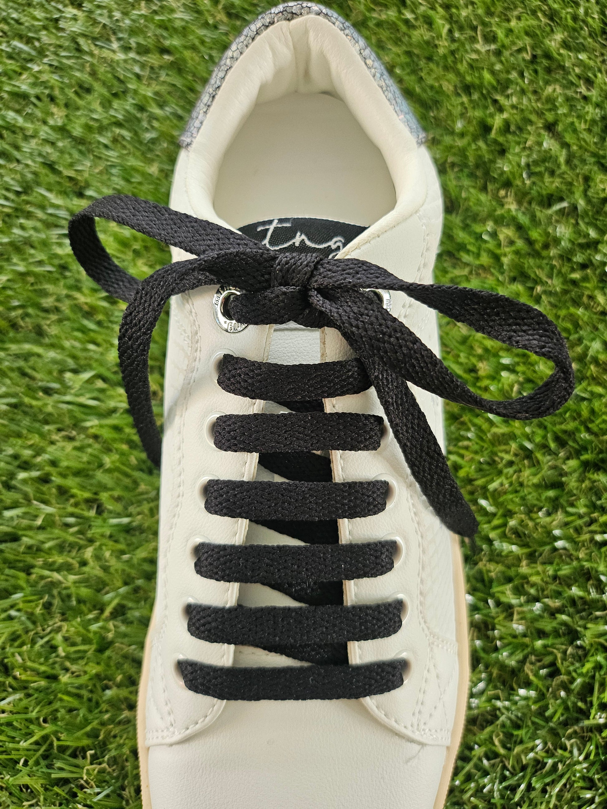 White sneaker with black shoelaces on a grass background