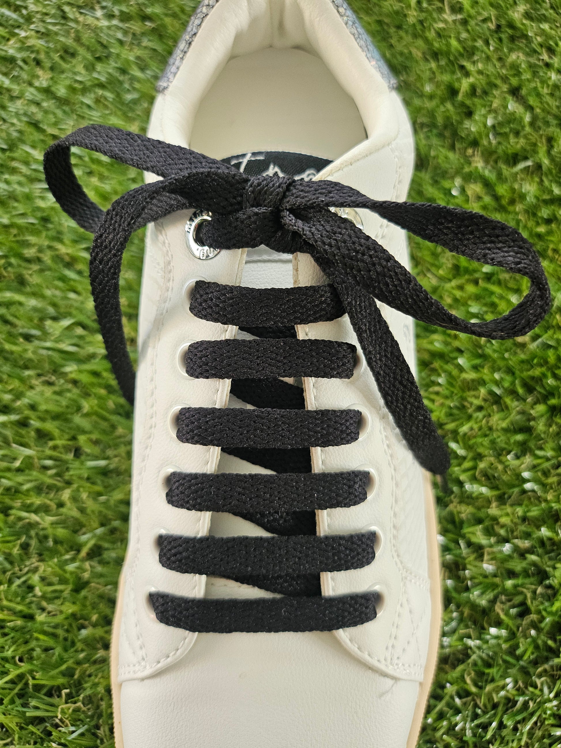 White sneaker with black shoelaces on a grass background