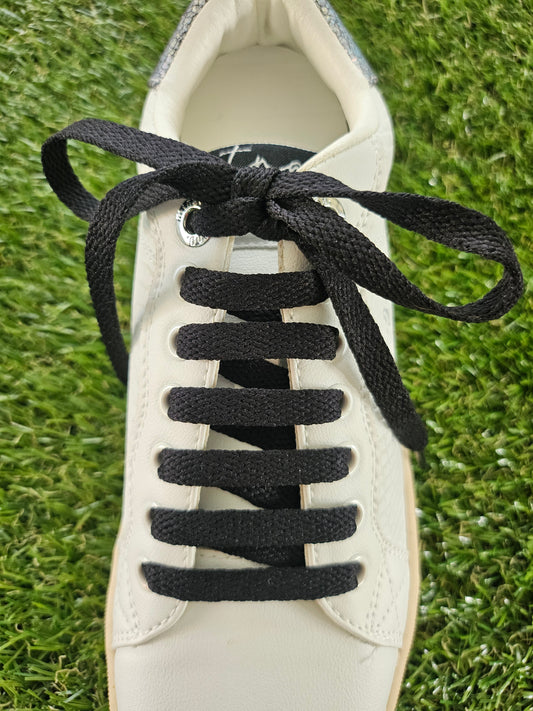 White sneaker with black shoelaces on a grass background