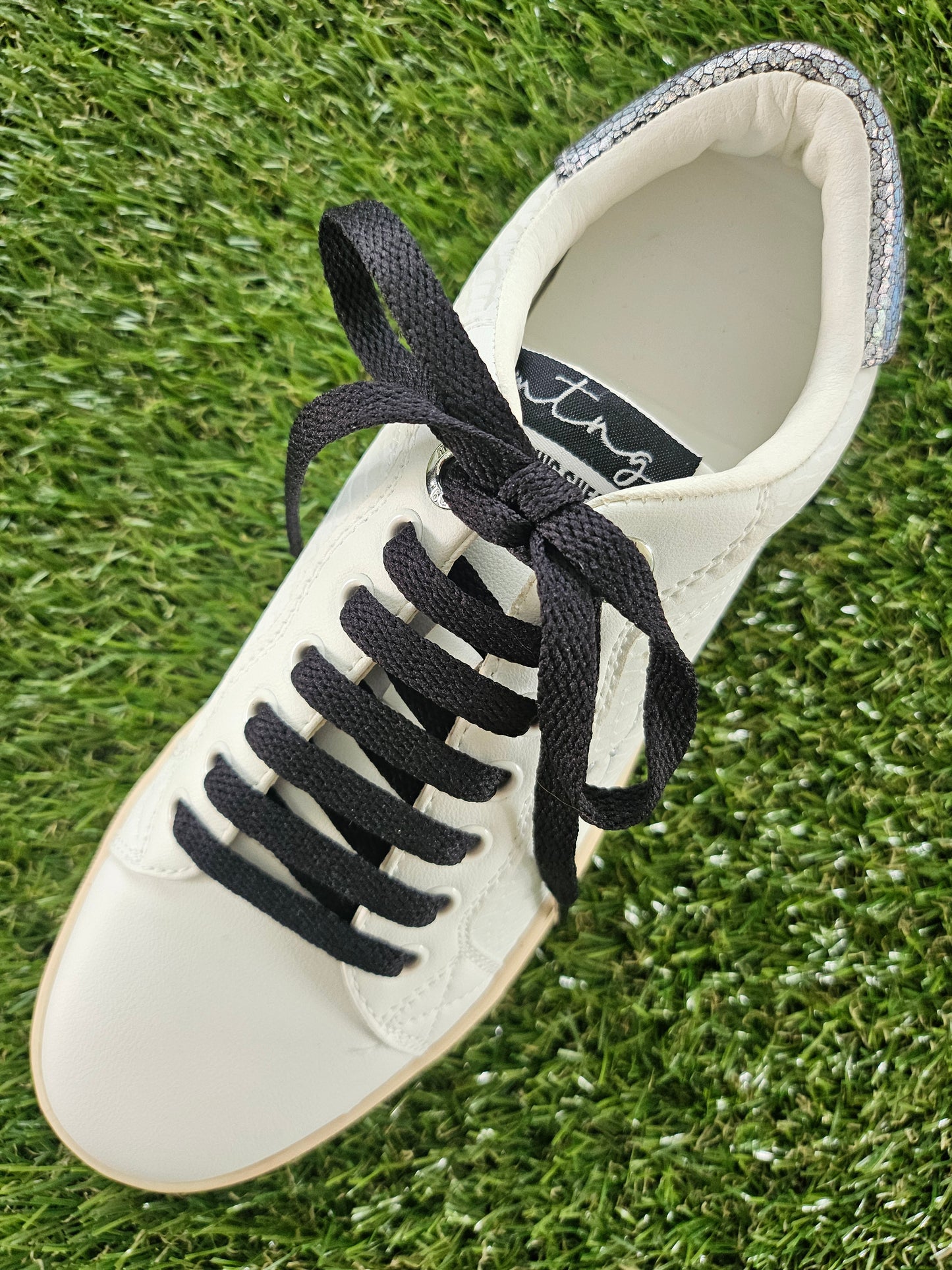 White sneaker with black laces on grass