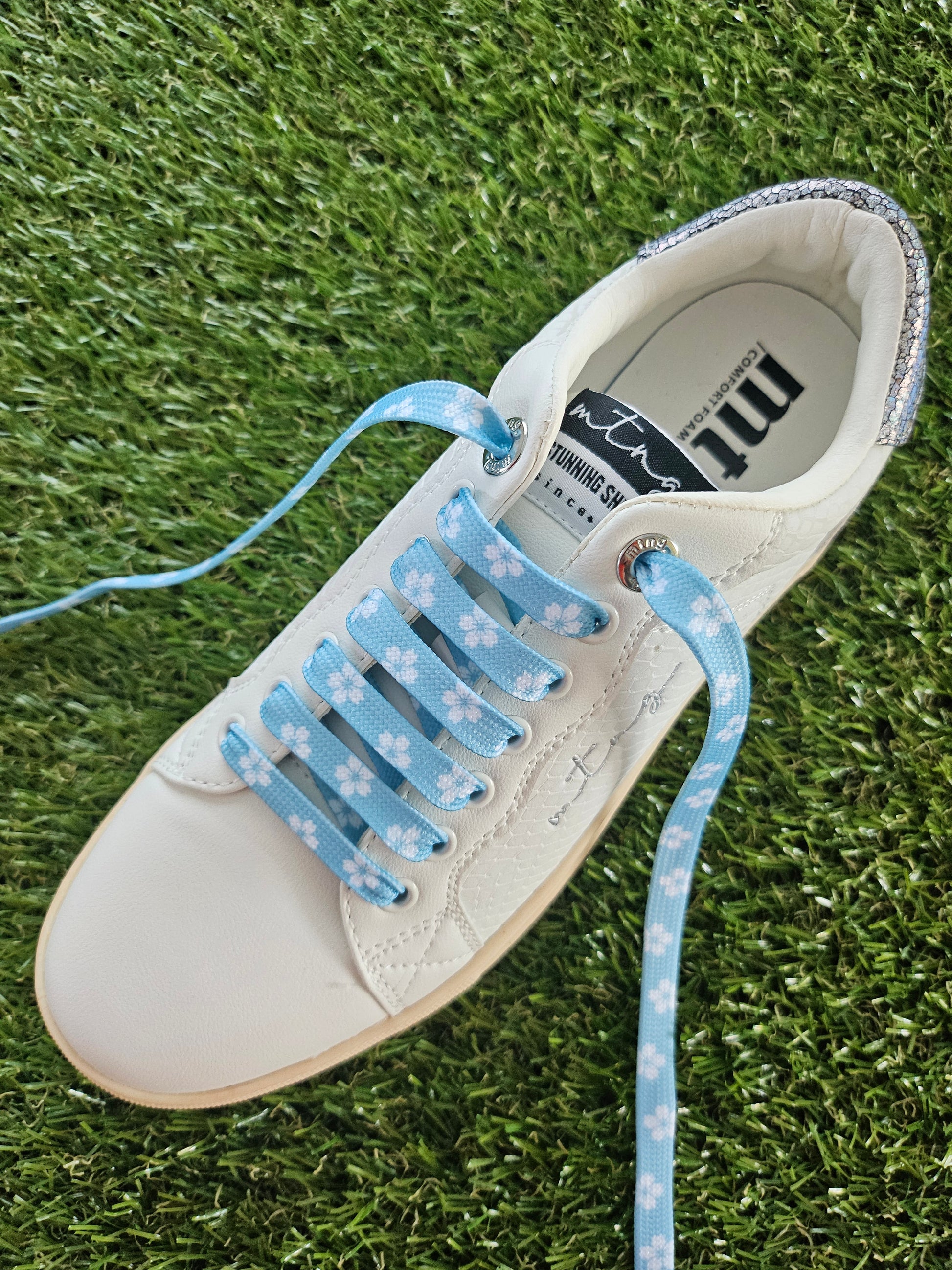 White sneaker with blue floral-patterned laces on grass