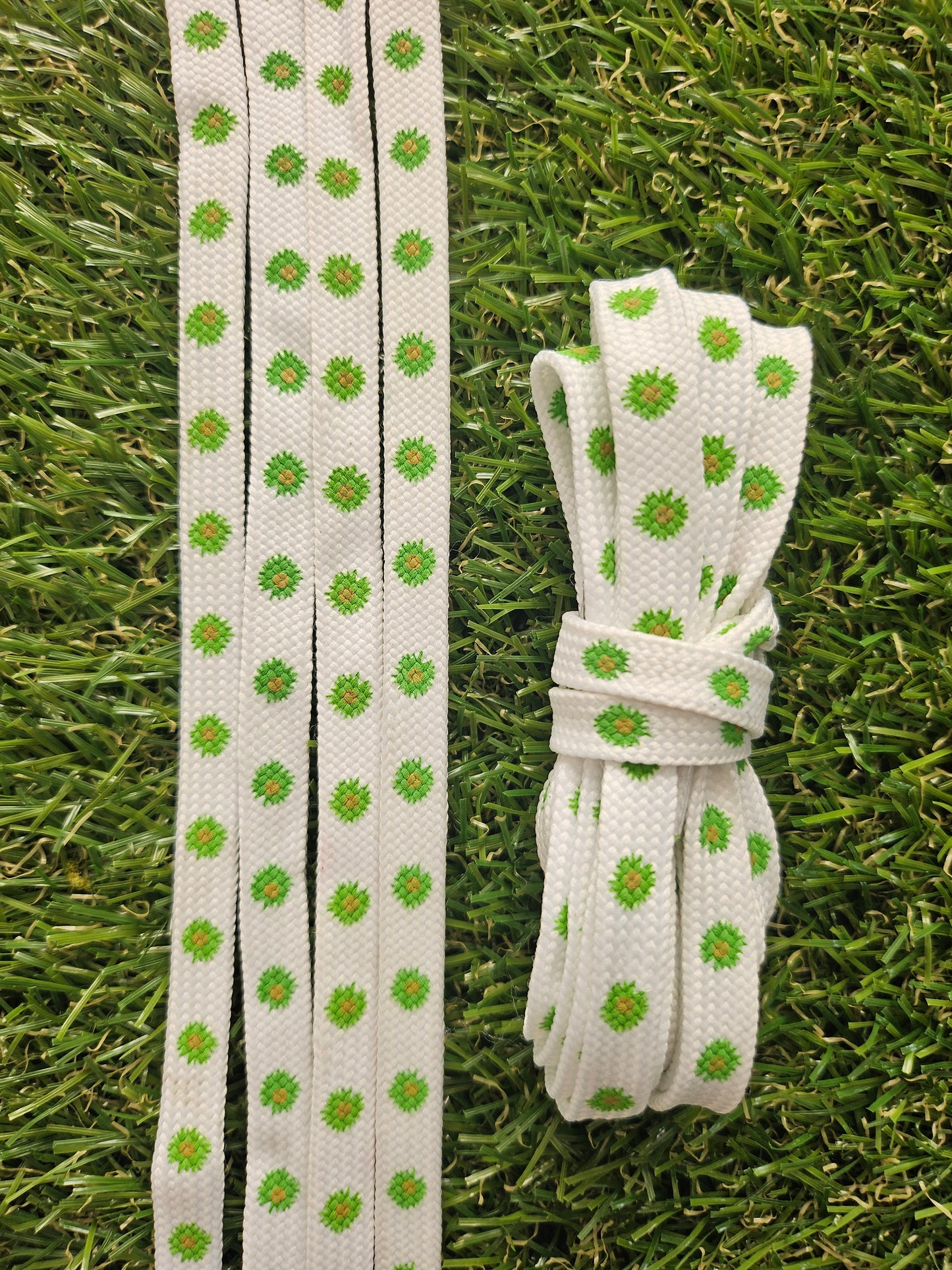 White shoelaces with green floral daisy patterns on grass