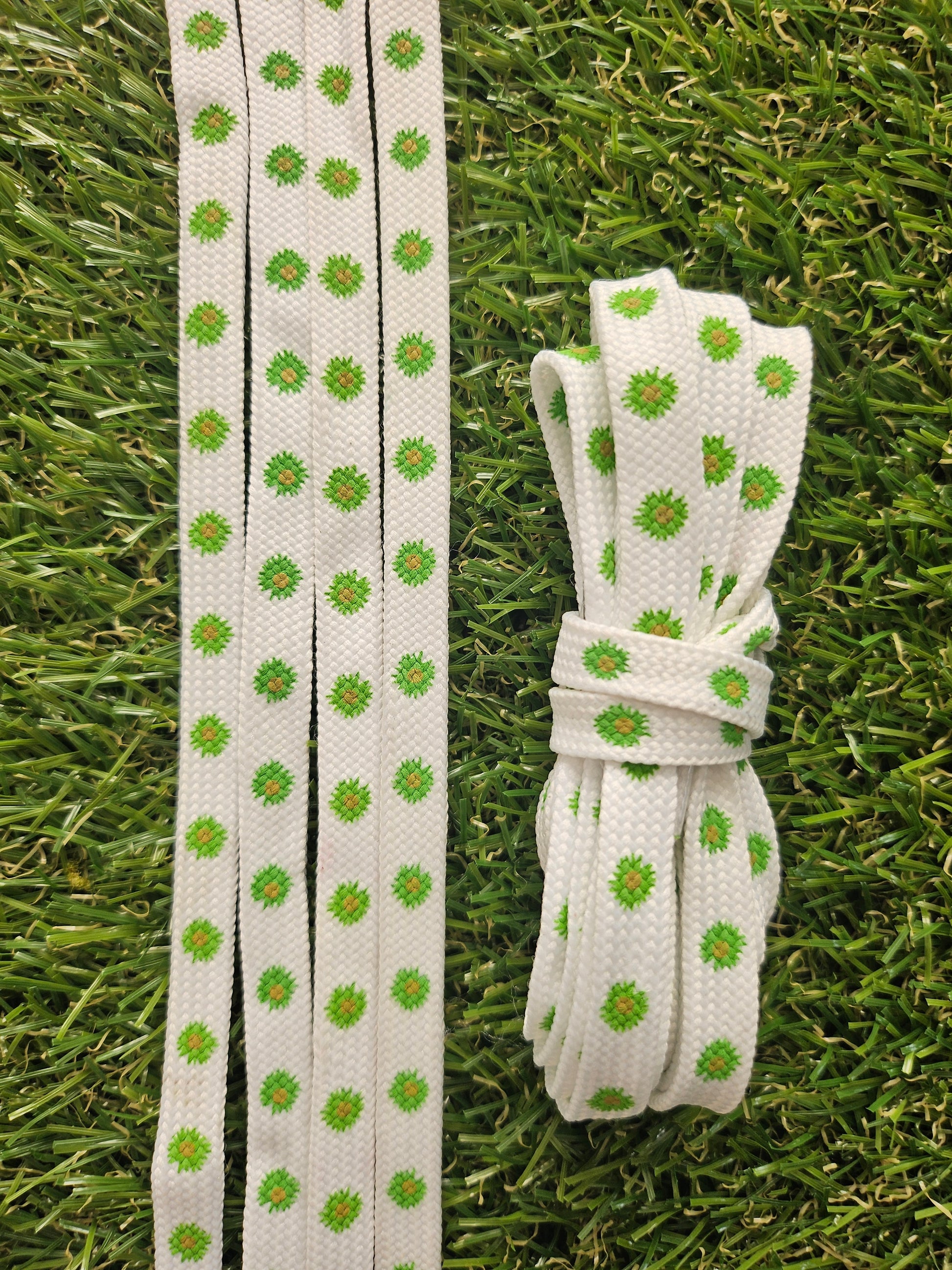 White shoelaces with green floral daisy patterns on grass