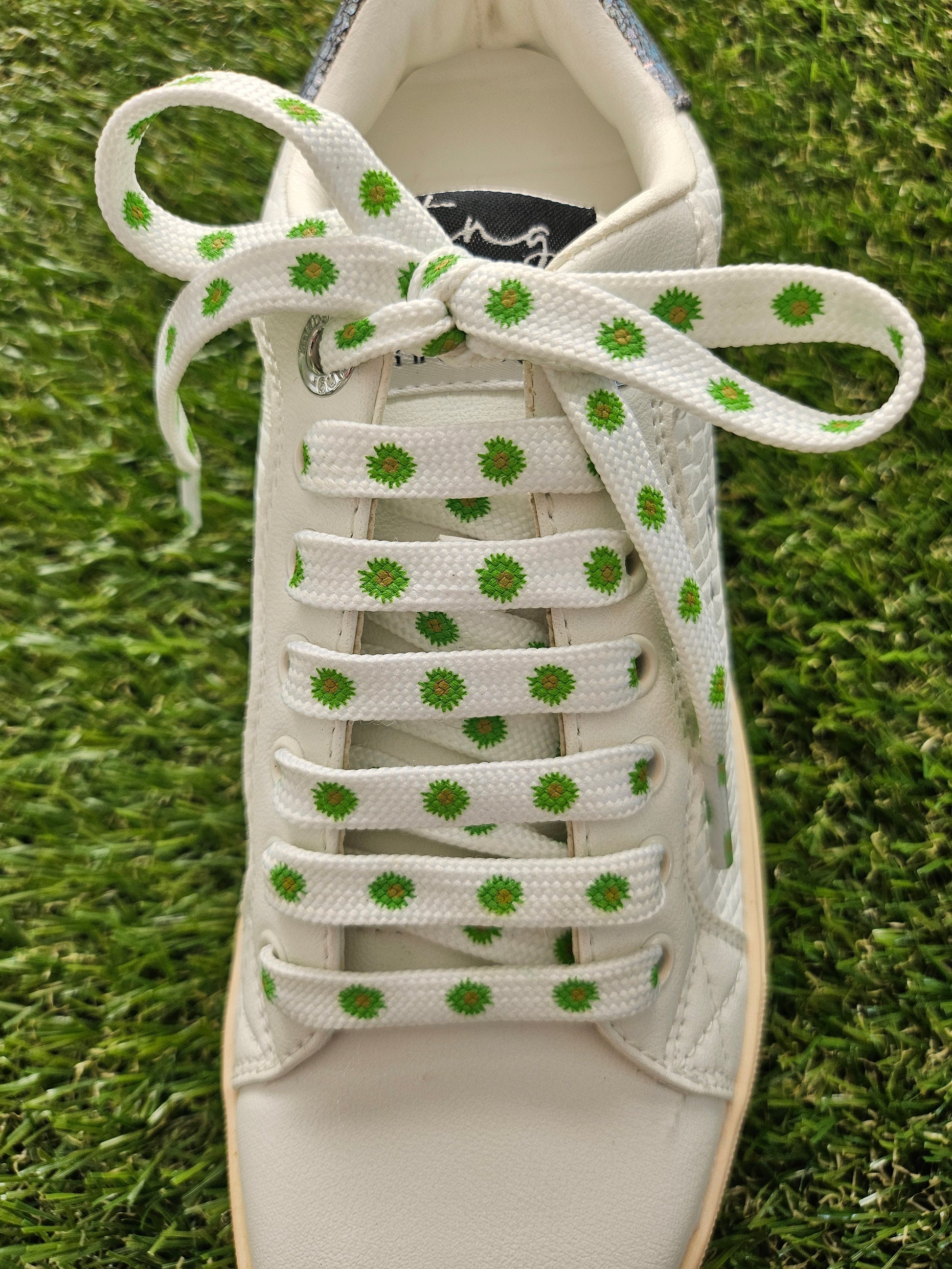 White sneaker with green patterned laces on grass