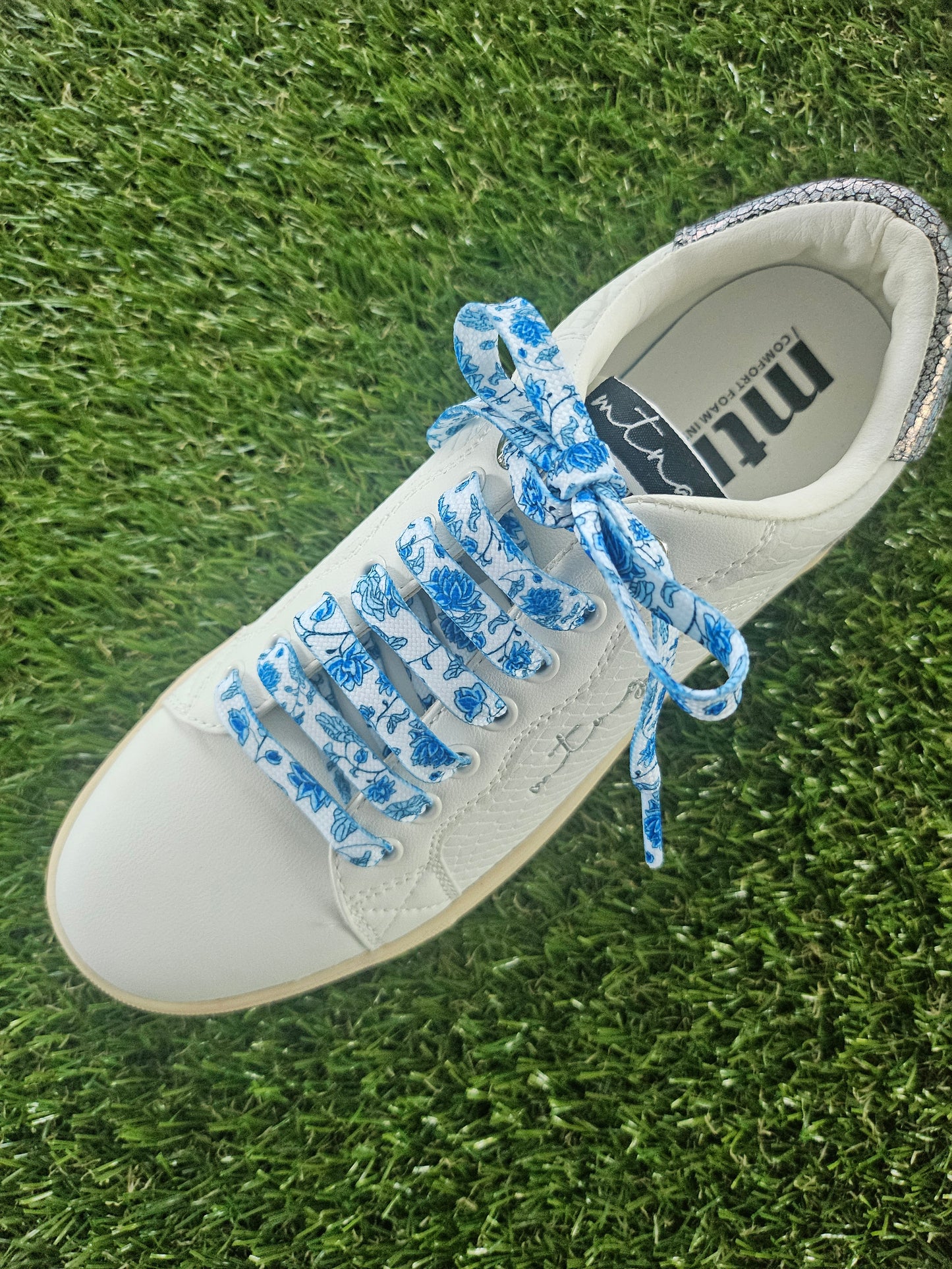 White sneaker with blue floral laces on grass
