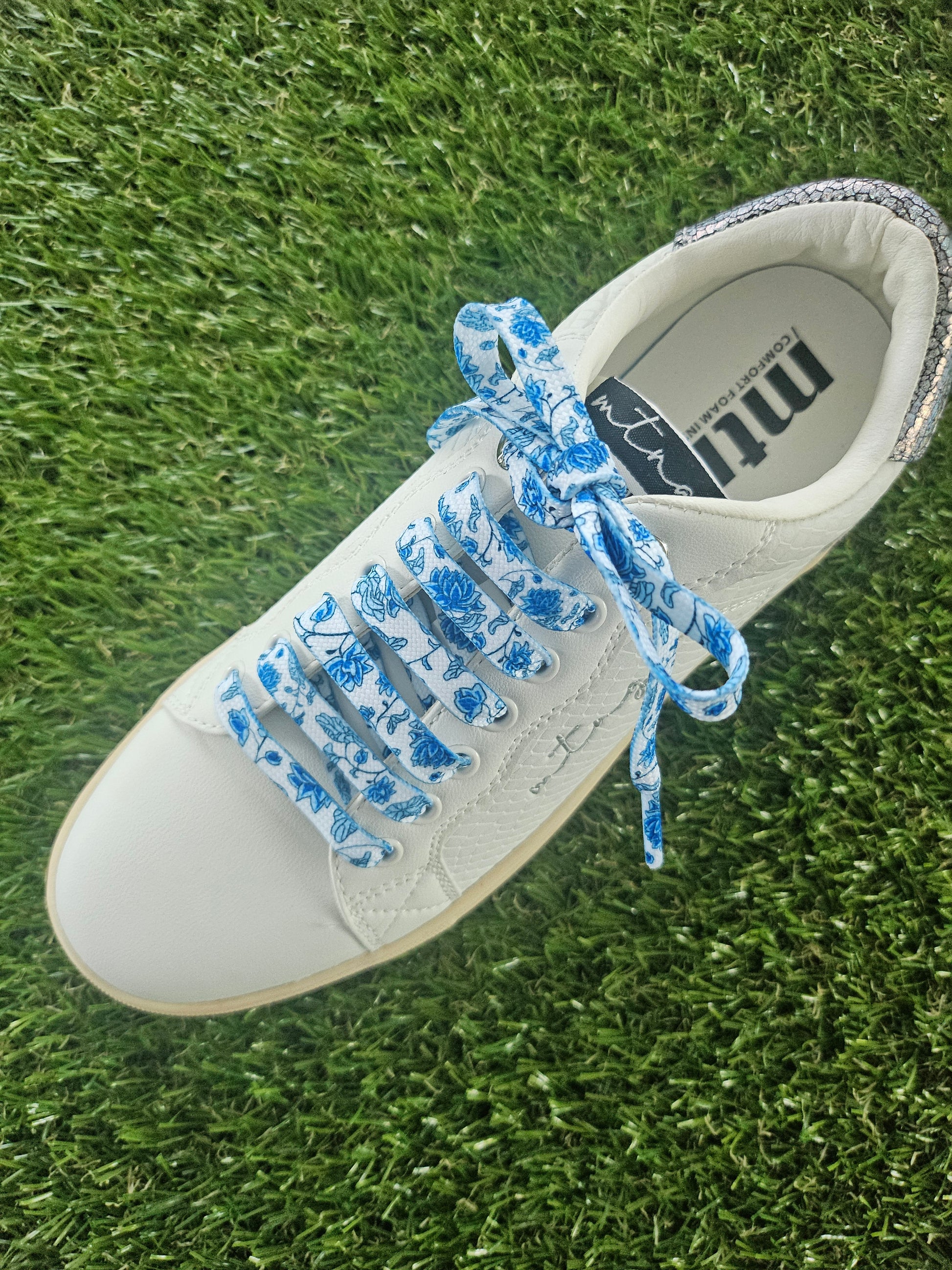 White sneaker with blue floral laces on grass